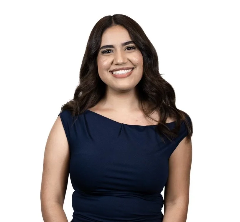 Smiling woman with long dark hair wearing a navy blue sleeveless top against a white background.