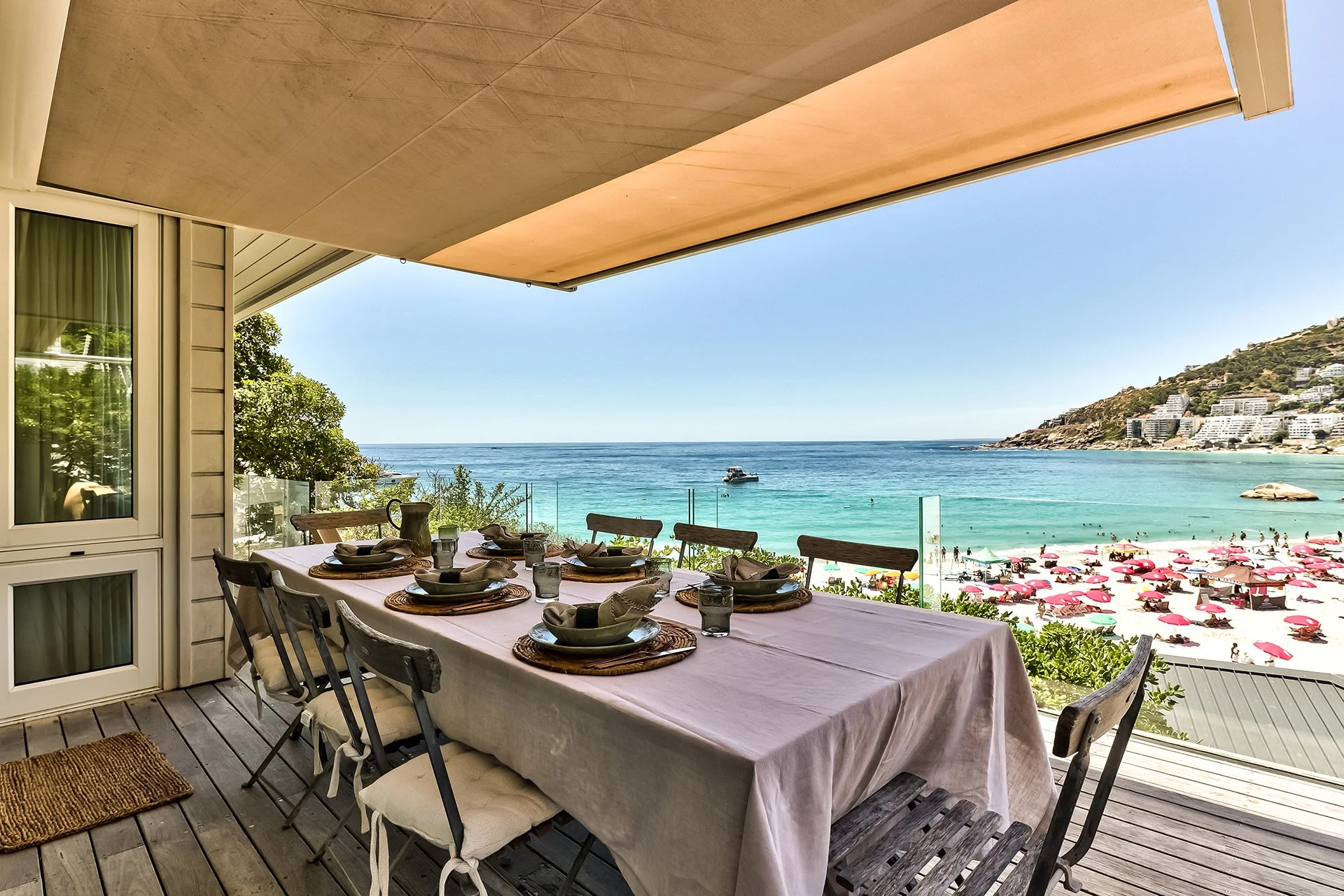 Long glass-walled beachfront deck with sunbeds and outdoor dining table for eight guests with braai, with BBQ area behind the kitchen. Direct access to beach down 40 steps.