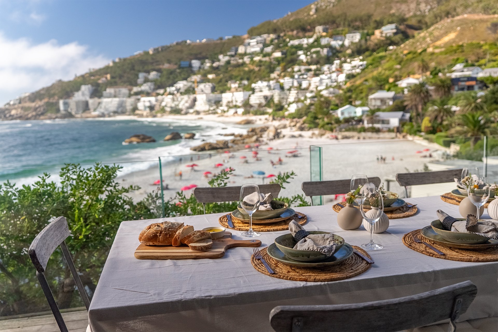Long glass-walled beachfront deck with sunbeds and outdoor dining table for eight guests with braai and BBQ area behind the kitchen. 