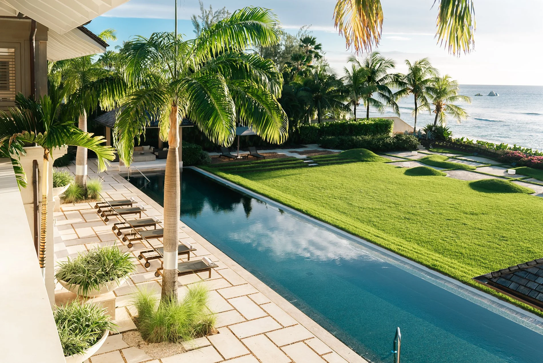 The sleek mosaic-lined pool is surrounded by limestone tiles and comfy sun loungers. Featuring large landscaped gardens with palm trees, scented shrubs and a spice garden. Escape to beachfront villa Godings with Simon Escapes.
