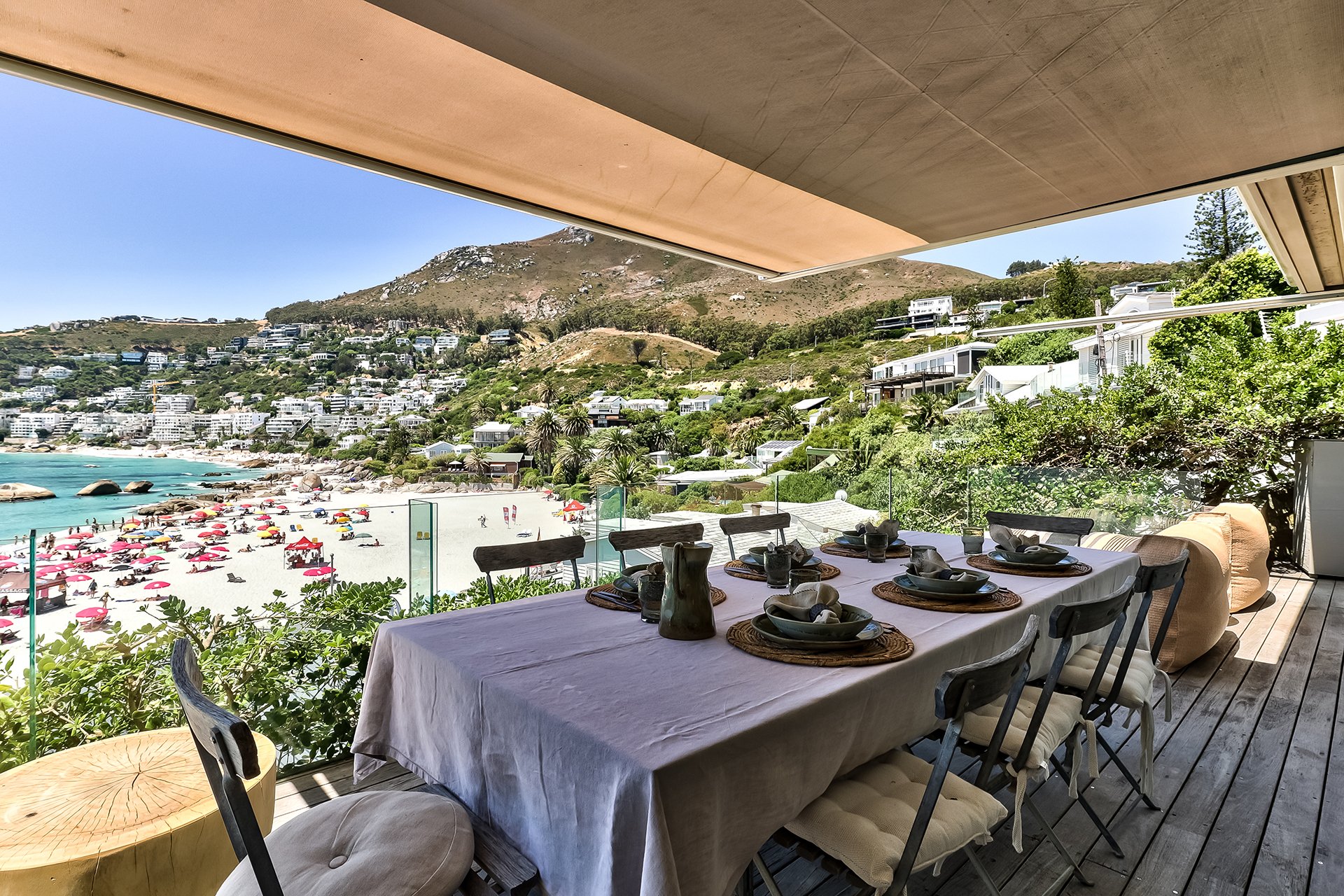 Long glass-walled beachfront deck with sunbeds and outdoor dining table for eight guests with braai and BBQ area behind the kitchen. Direct access to beach down 40 steps. Make an enquiry for a Cape Town luxury escape. 