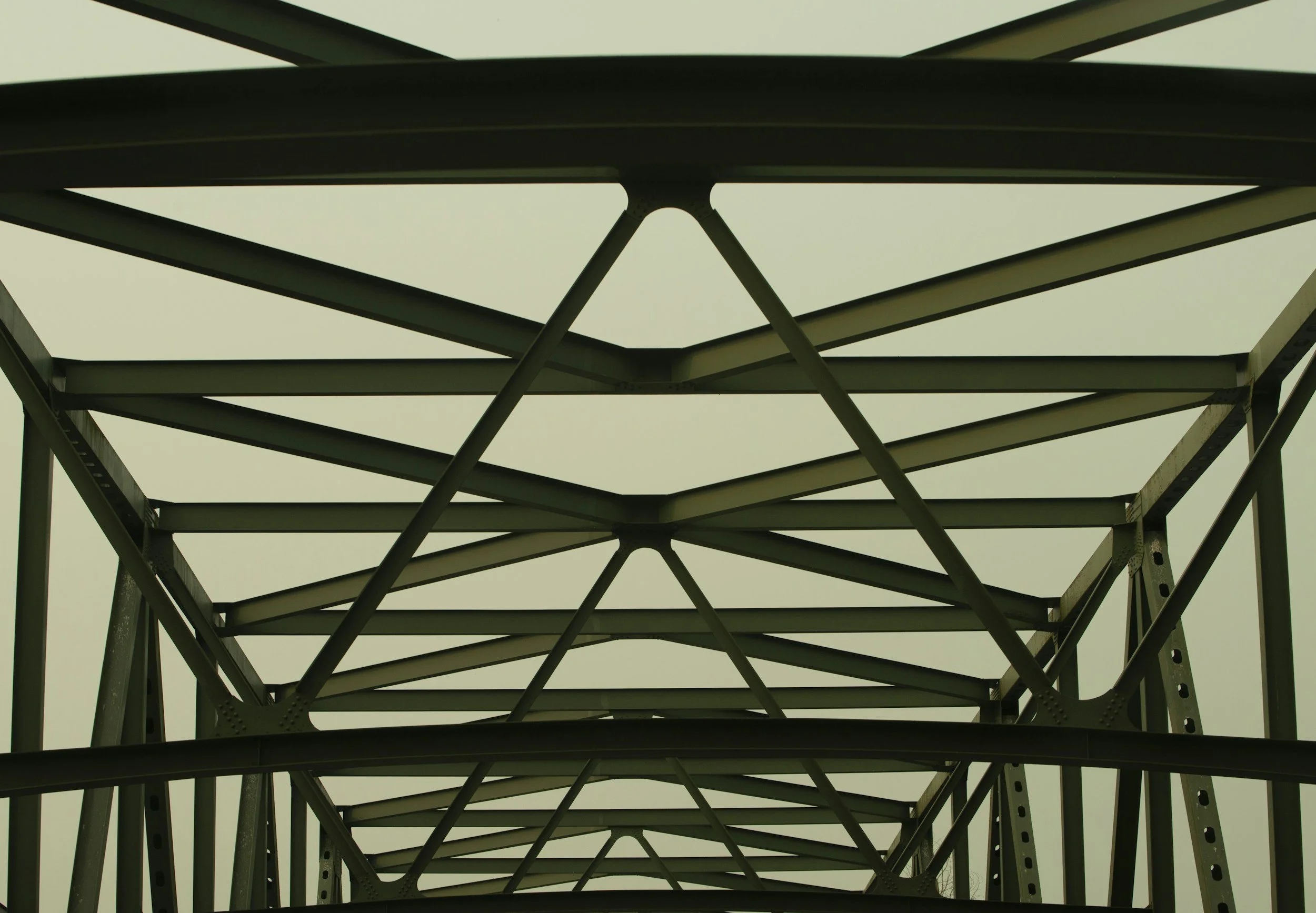 Looking up at the underside of a metal bridge or tower structure showing interconnected beams and supports.