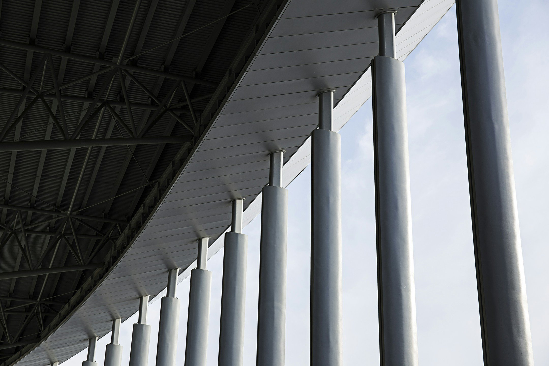 Close-up of modern architectural structure with vertical metal columns supporting an overhang against a cloudy sky.