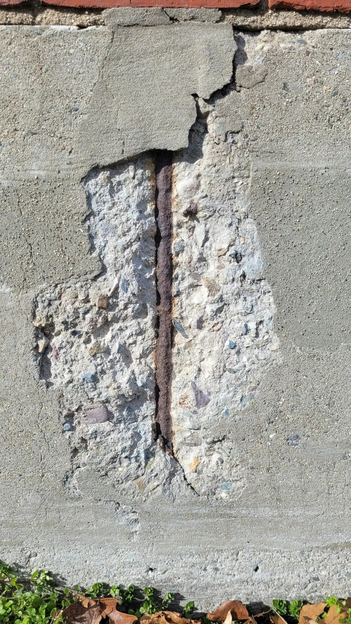 Close-up of a cracked and damaged concrete and brick wall.