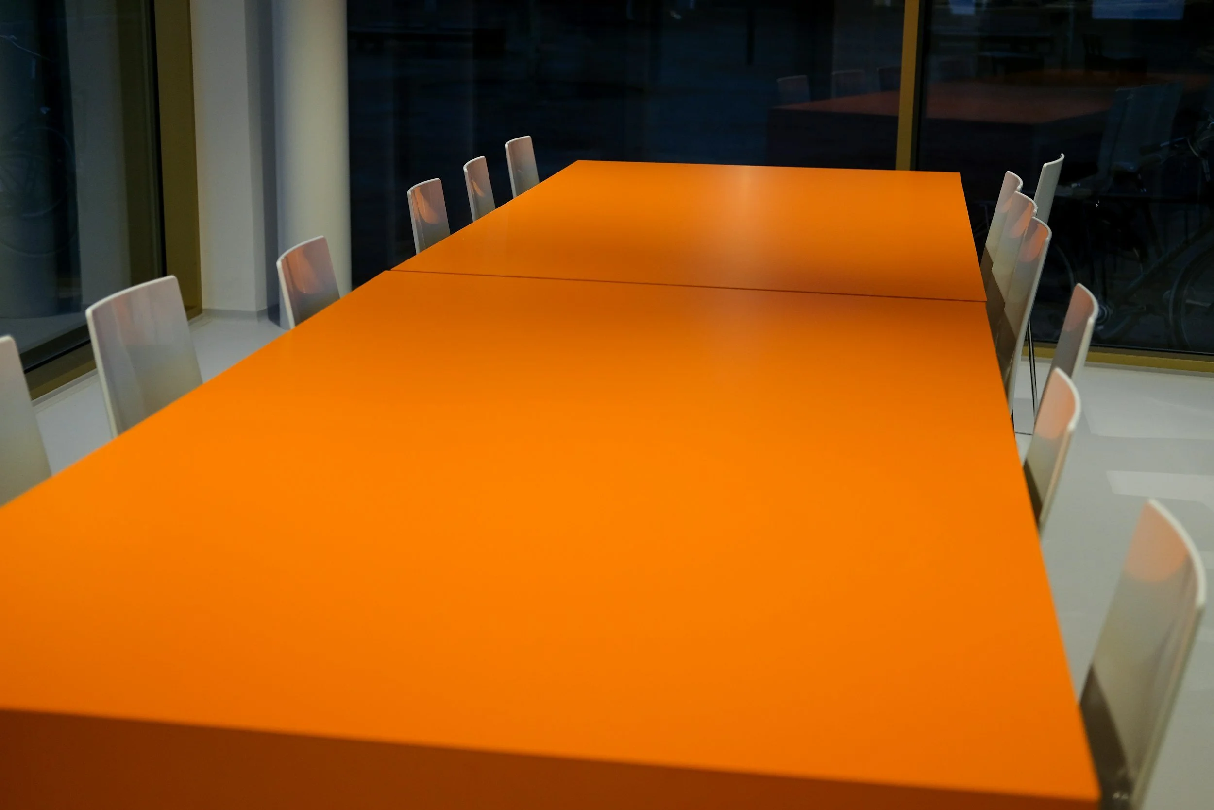 An orange conference table with white chairs around it in a modern office.