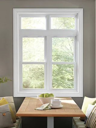 L-shaped window with white frame, overlooking green trees outside, with a wooden table below it.