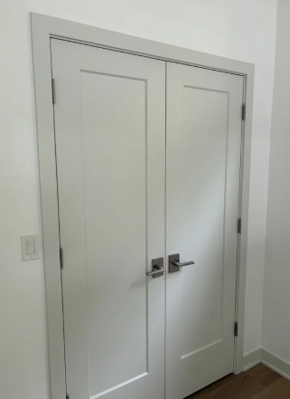 A pair of closed white double doors with silver handles in a room with white walls and wood flooring.