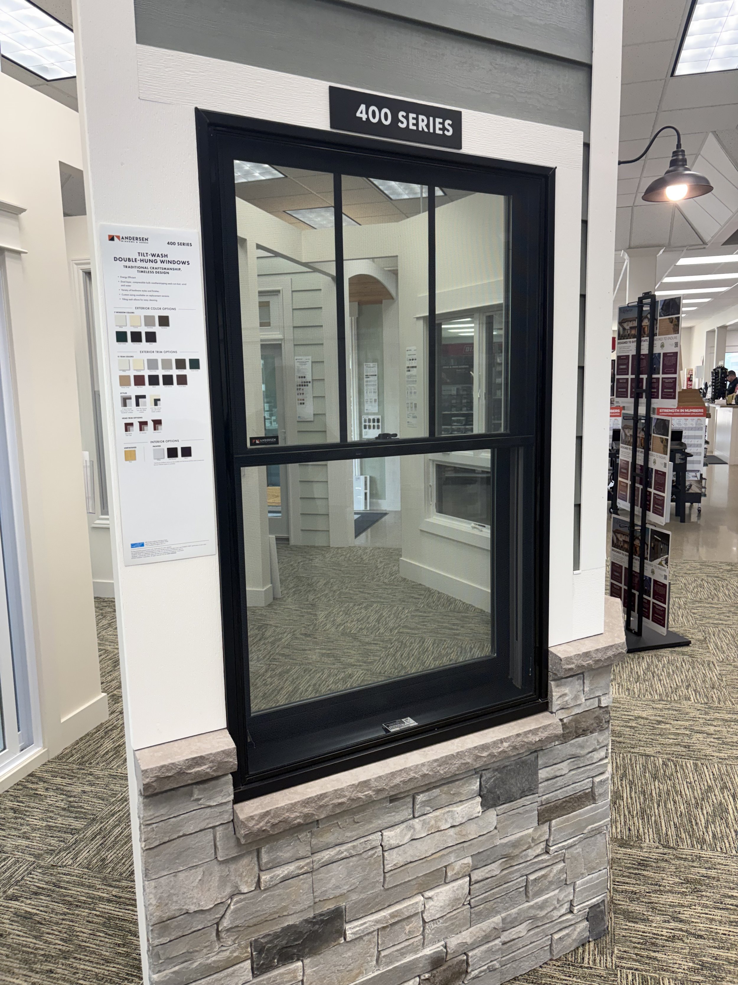 Display of a black-framed window with a stone base in a showroom, with a sign above labeled '400 Series' and interior windows and options visible inside.