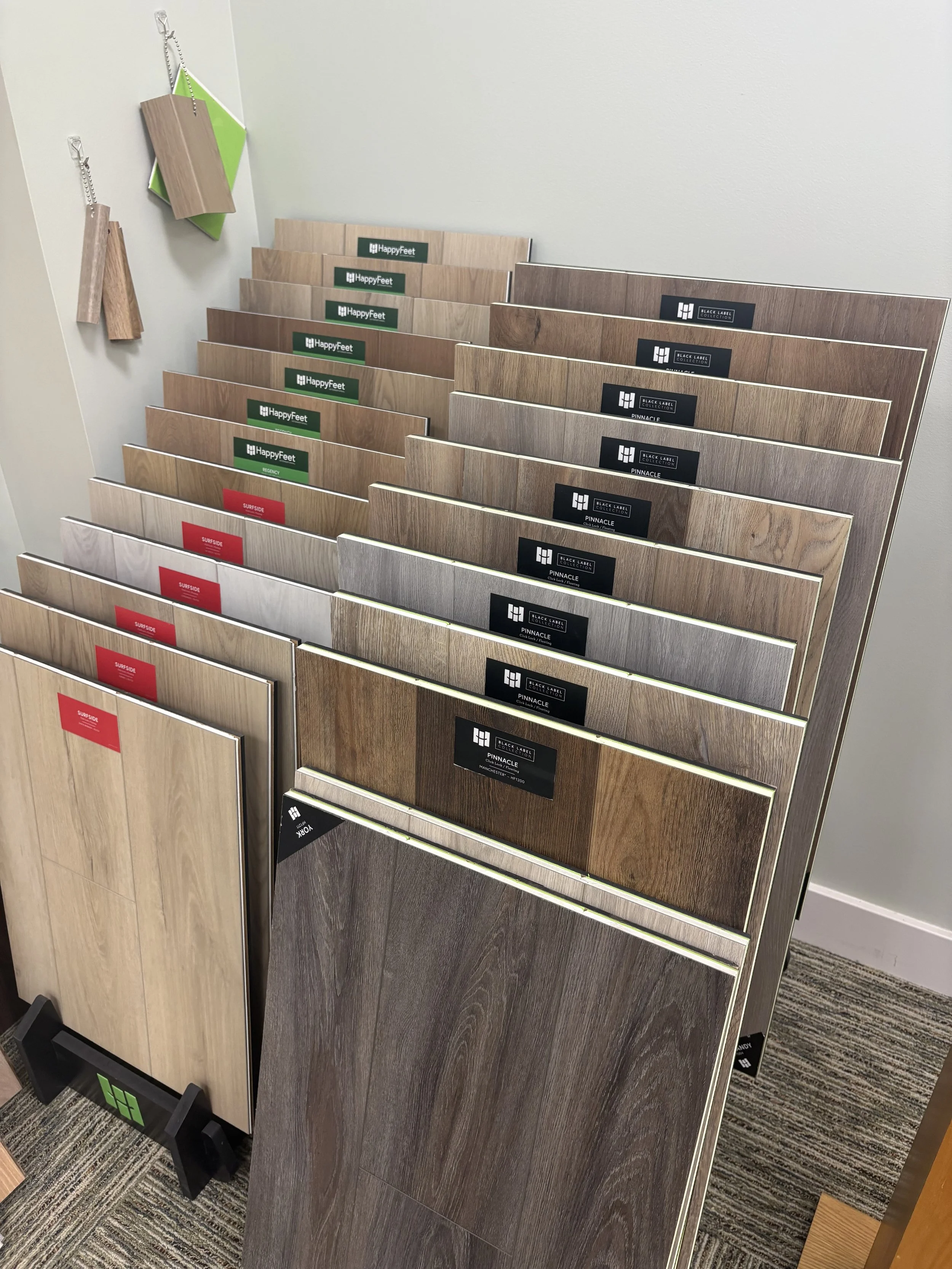 Display of different wood flooring samples, arranged in a stand with labels such as HappyFeet, Black Label Collection, and Surfside.
