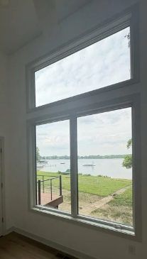 View through a large window of a river or lake with boats and greenery on the shore.