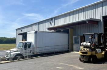 Delivery truck parked outside a warehouse with a forklift nearby.