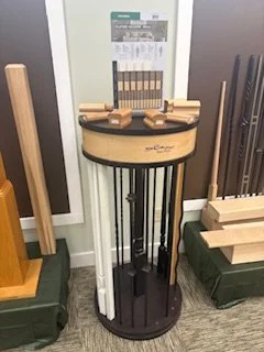 Display stand with sample wood stains or finishes and color chart, surrounded by wood samples and equipment in a workshop.