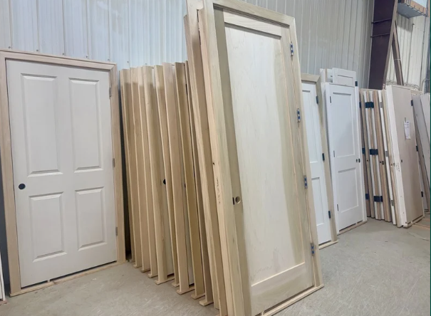 Various white primed and cased interior doors leaning against a wall in a warehouse or storage area.