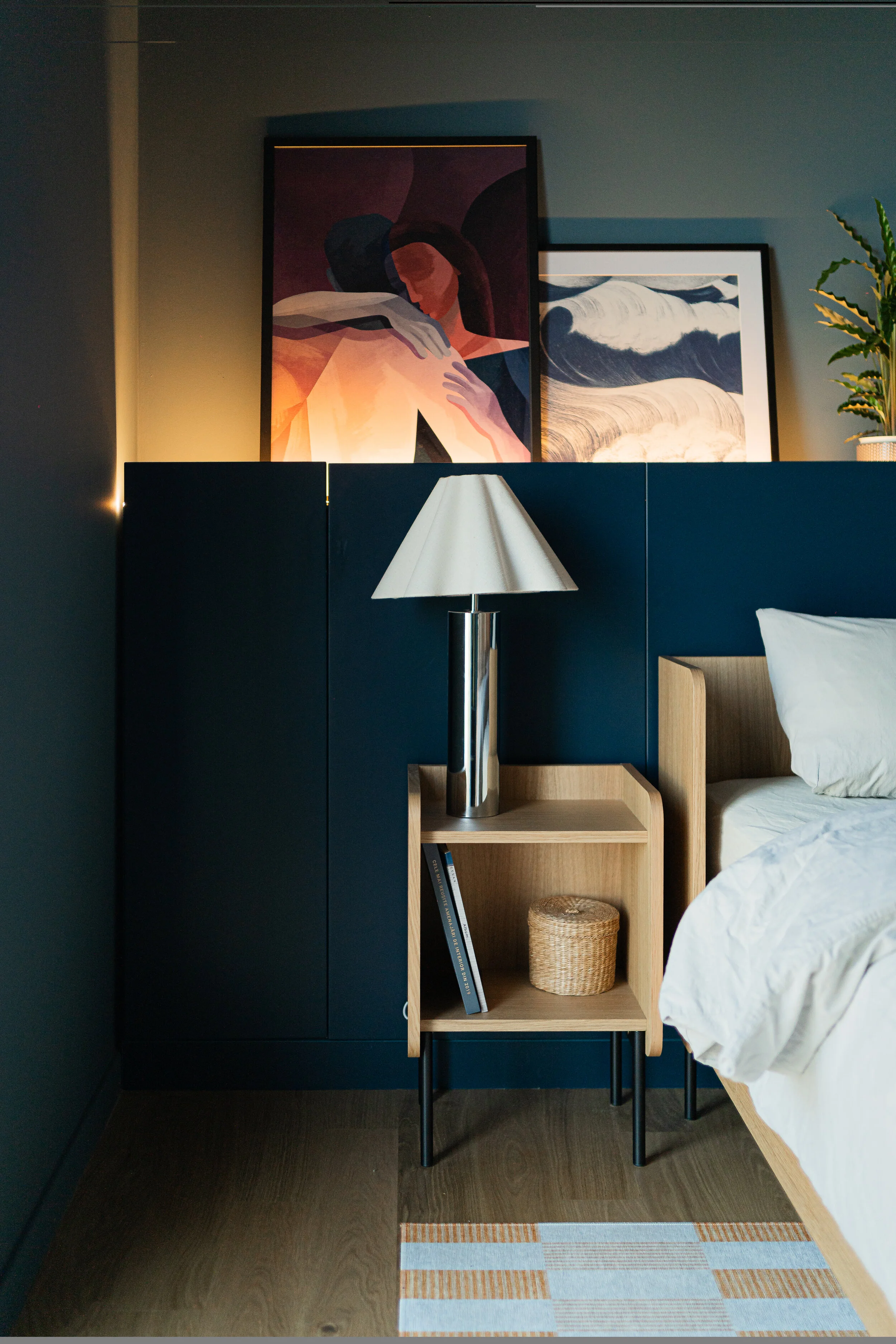 Modern bedroom with a bed, pillows, abstract art above, bedside tables, lamp, and ceiling light, with a striped rug.