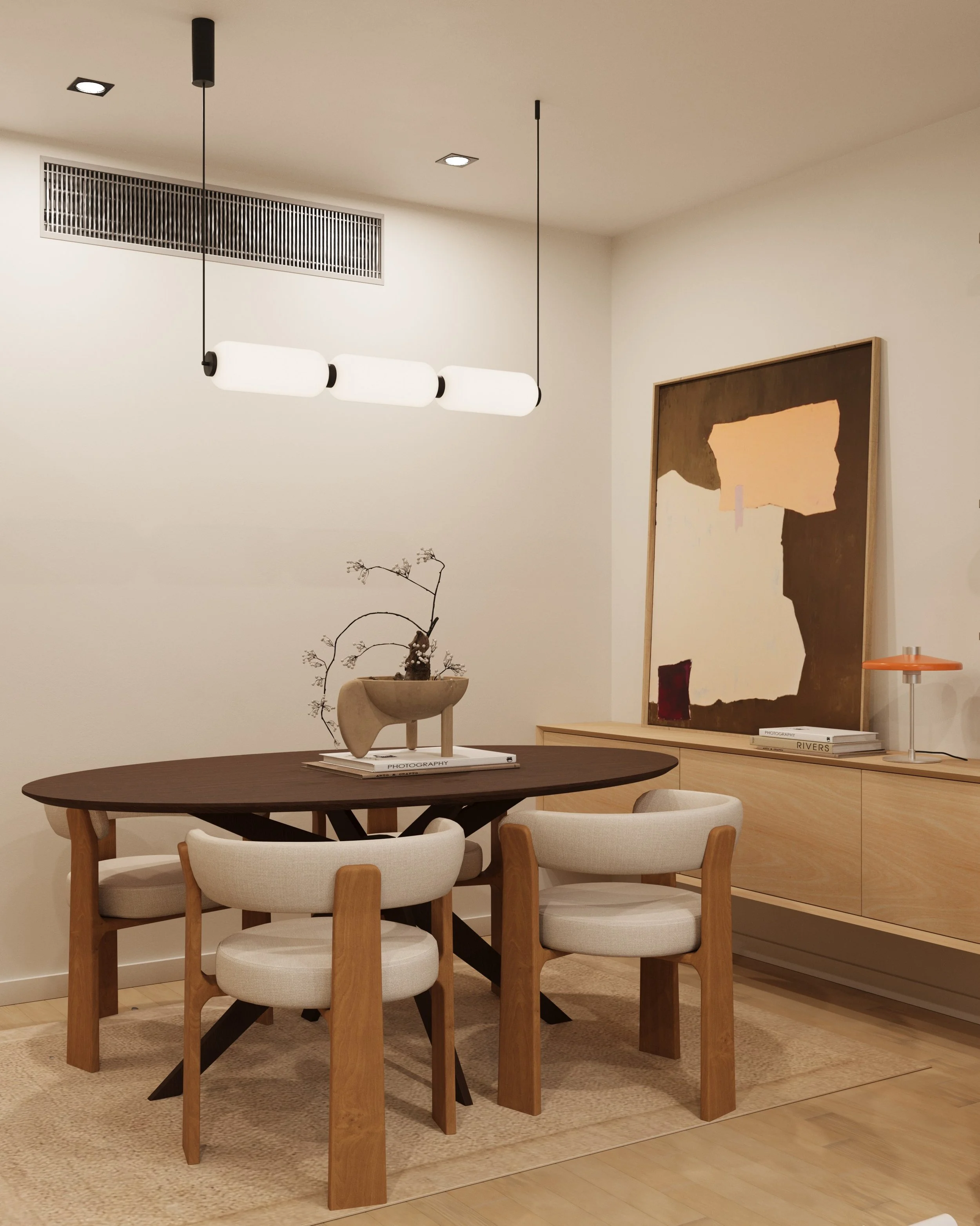 A round wooden table with four upholstered chairs around it, a black and white patterned rug underneath, and a large abstract painting with earthy tones on the wall beside a small table with a stack of magazines, a blue rolled-up yoga mat, and a white box of photography-related books.
