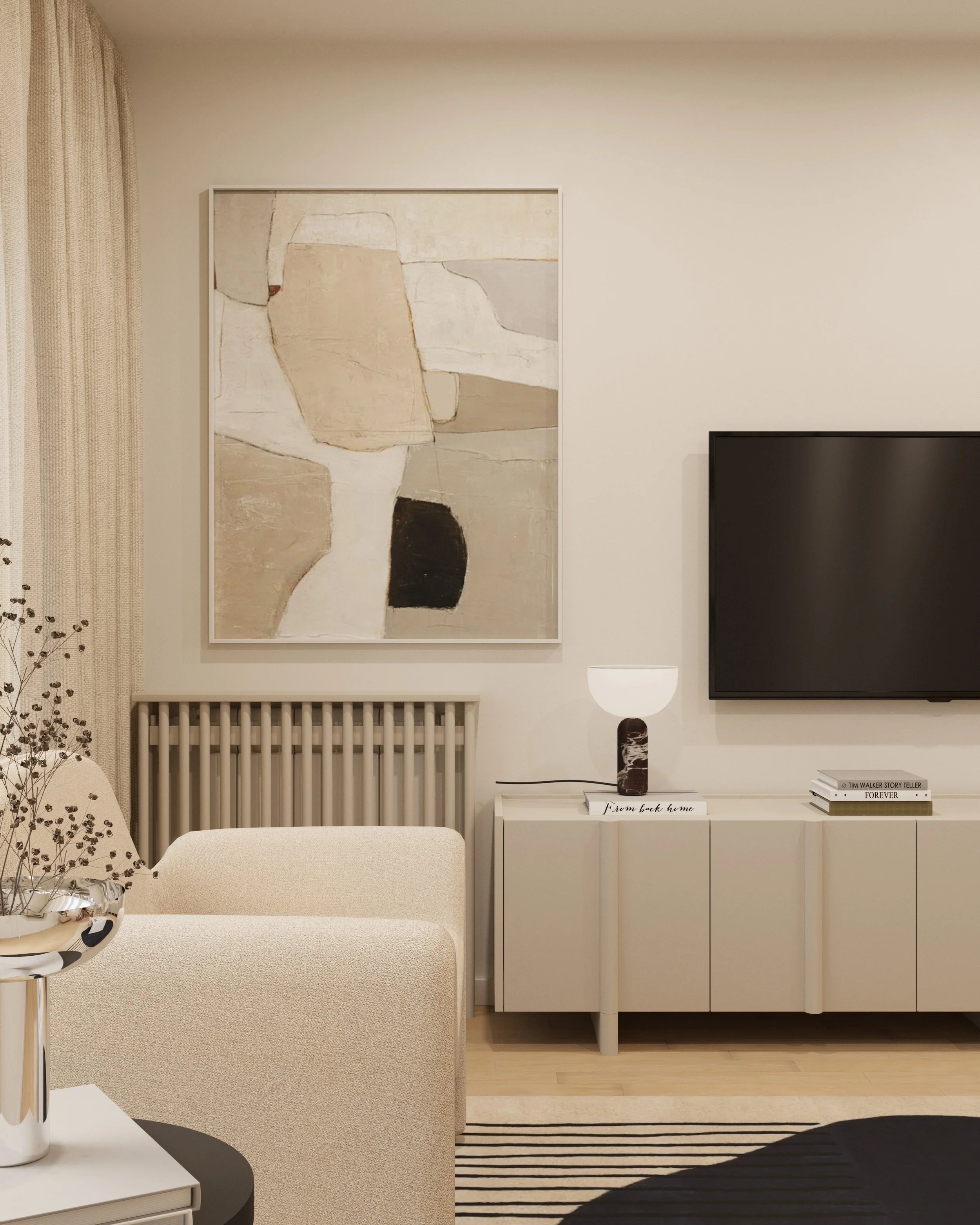Minimalist living room with a large flat-screen TV mounted on a white wall, decorated with a modern black and silver wall sculpture. A white sideboard below holds decorative books, a white vase with dried flowers, and candles on a tray. There is a white chair with a rounded back and a small, round side table. The floor is light wood, and the room has soft, neutral tones.