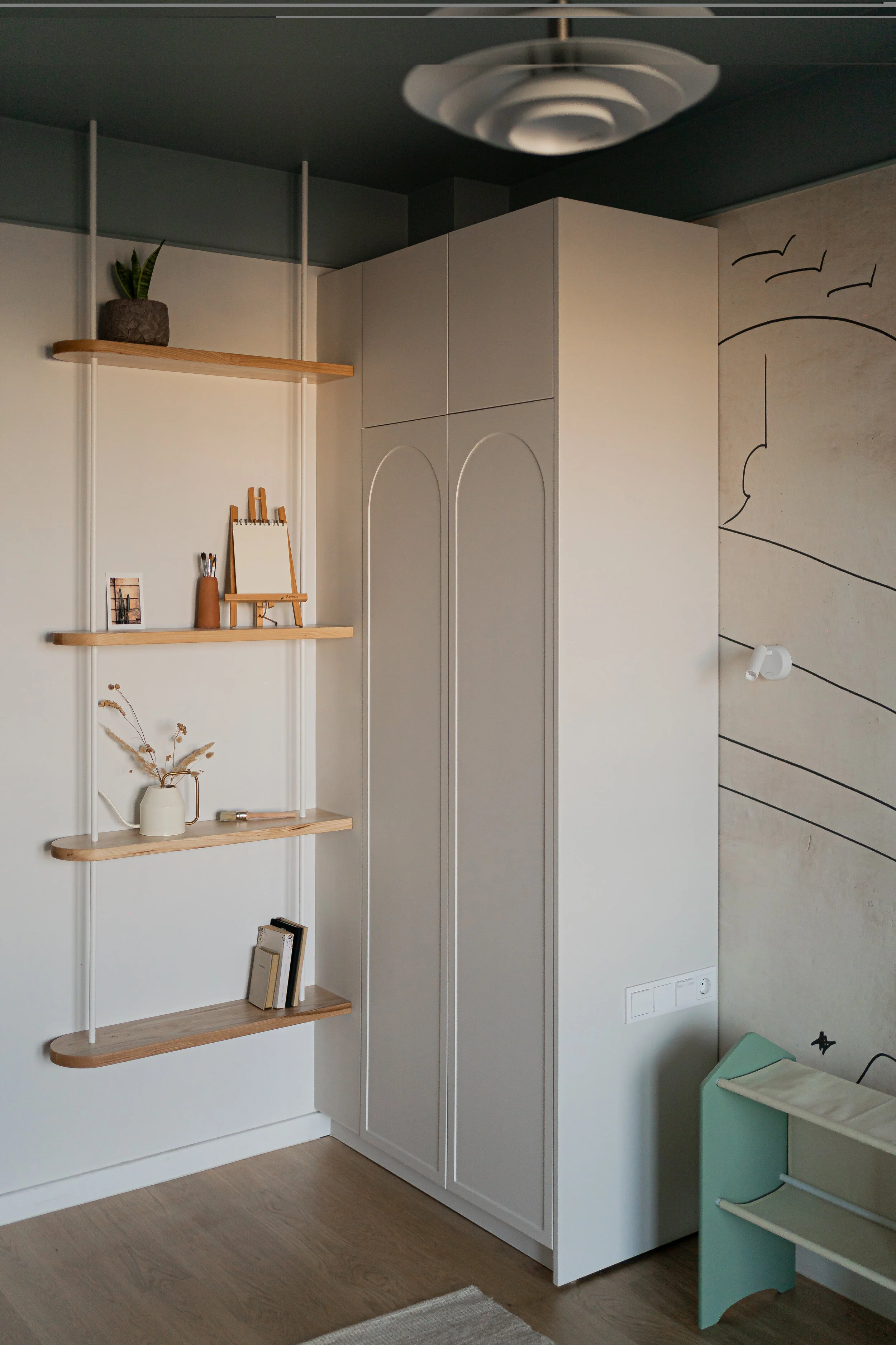 Modern living room with a beige sofa, gray and black pillows, a cream-colored knitted blanket, a pink side table, a geometric light fixture, and wall art with abstract black line drawings.