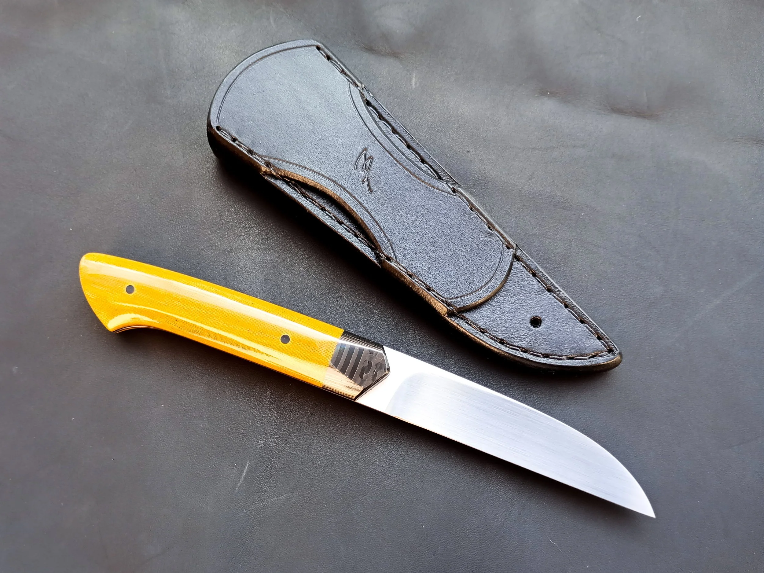 A fixed-blade knife with a yellow handle and a black leather sheath