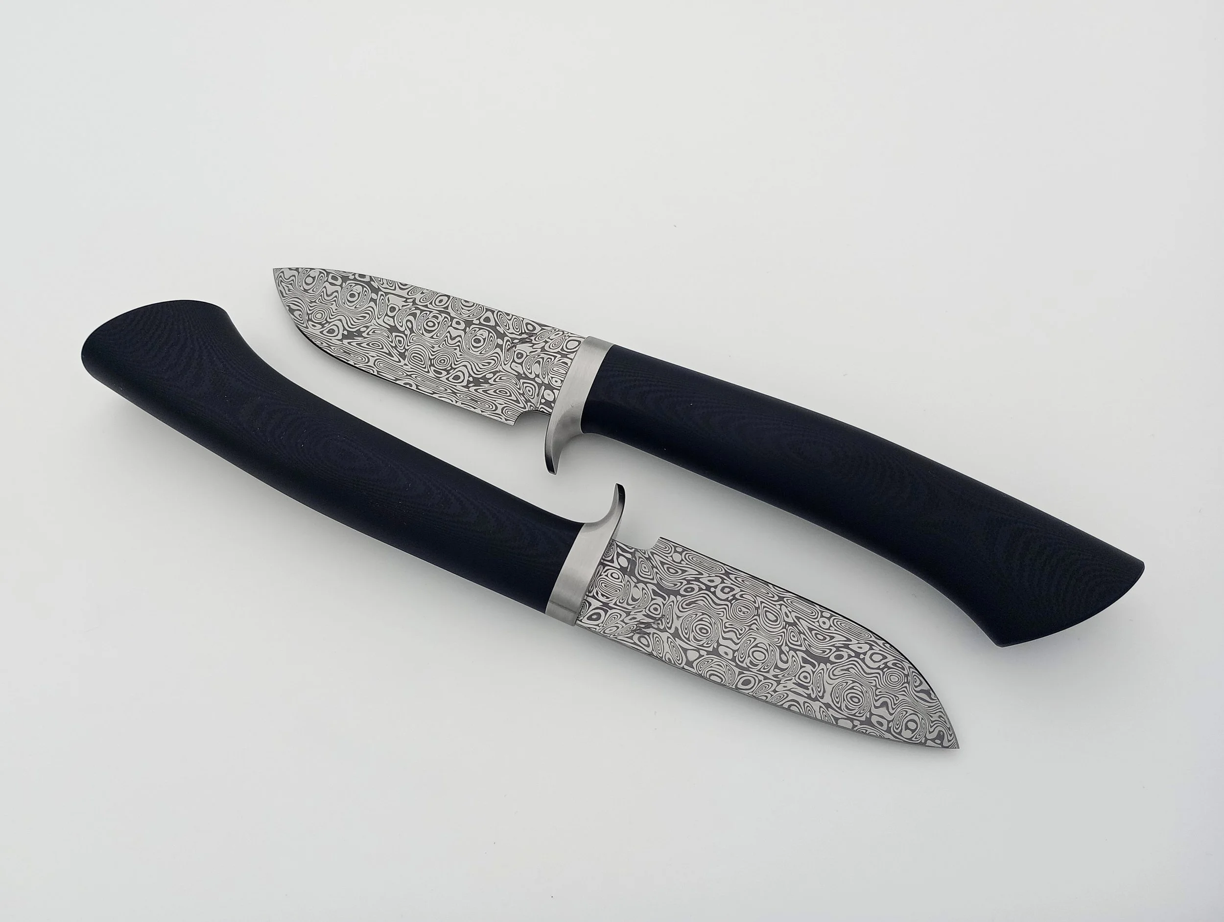 Two Damascus steel knives with black handles.