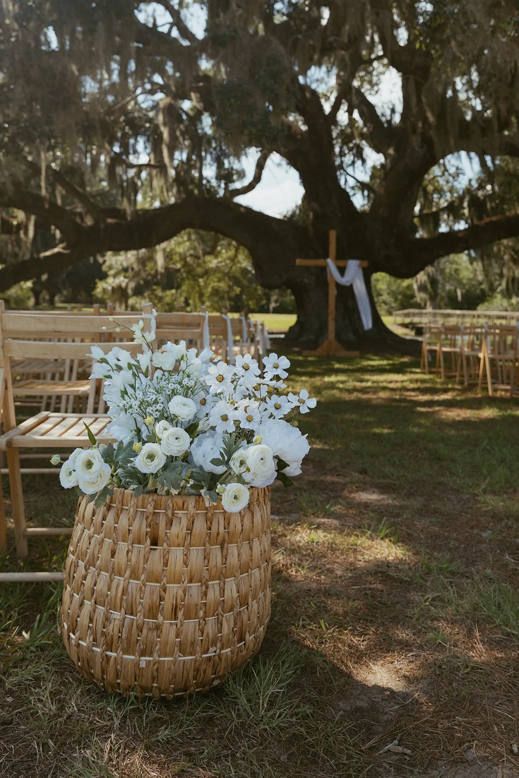 Wedding ceremony setup beneath historic moss-covered live oak at Agapae Oaks St. Helena Island South Carolina featuring aisle floral arrangement and Southern outdoor ceremony styling at Lowcountry destination wedding venue.