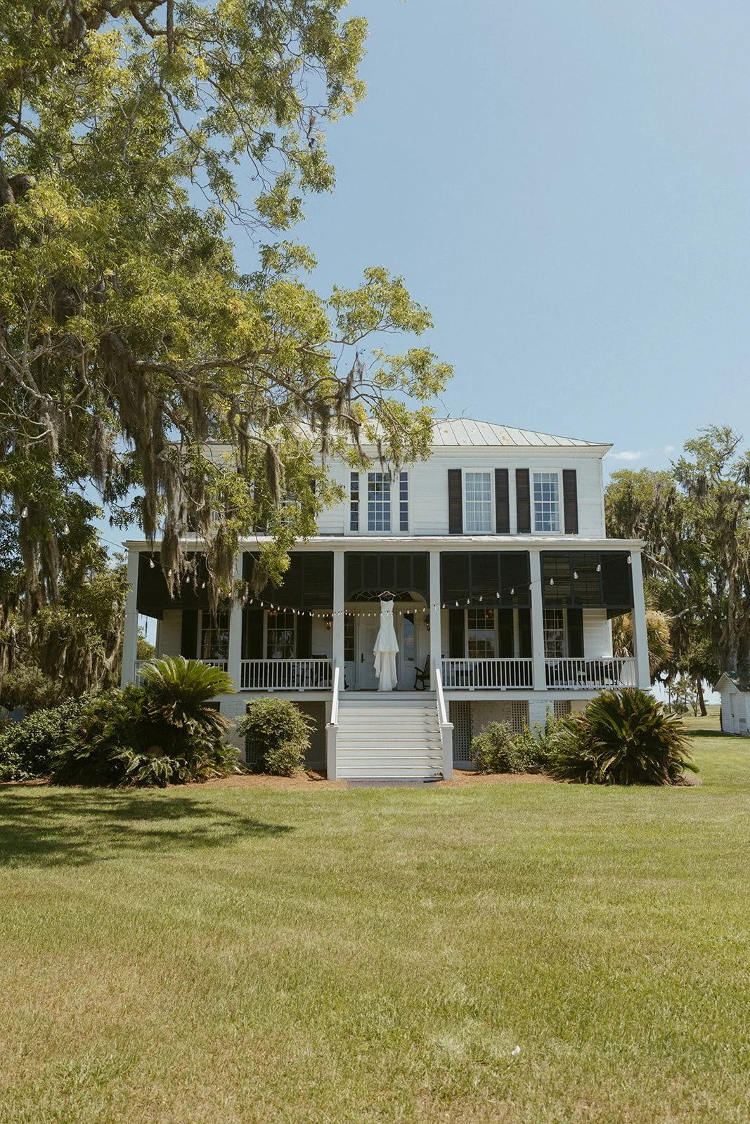 Historic Southern estate at Agapae Oaks St. Helena Island South Carolina with wedding dress displayed on front porch beneath moss-covered oak trees at Lowcountry destination wedding venue.