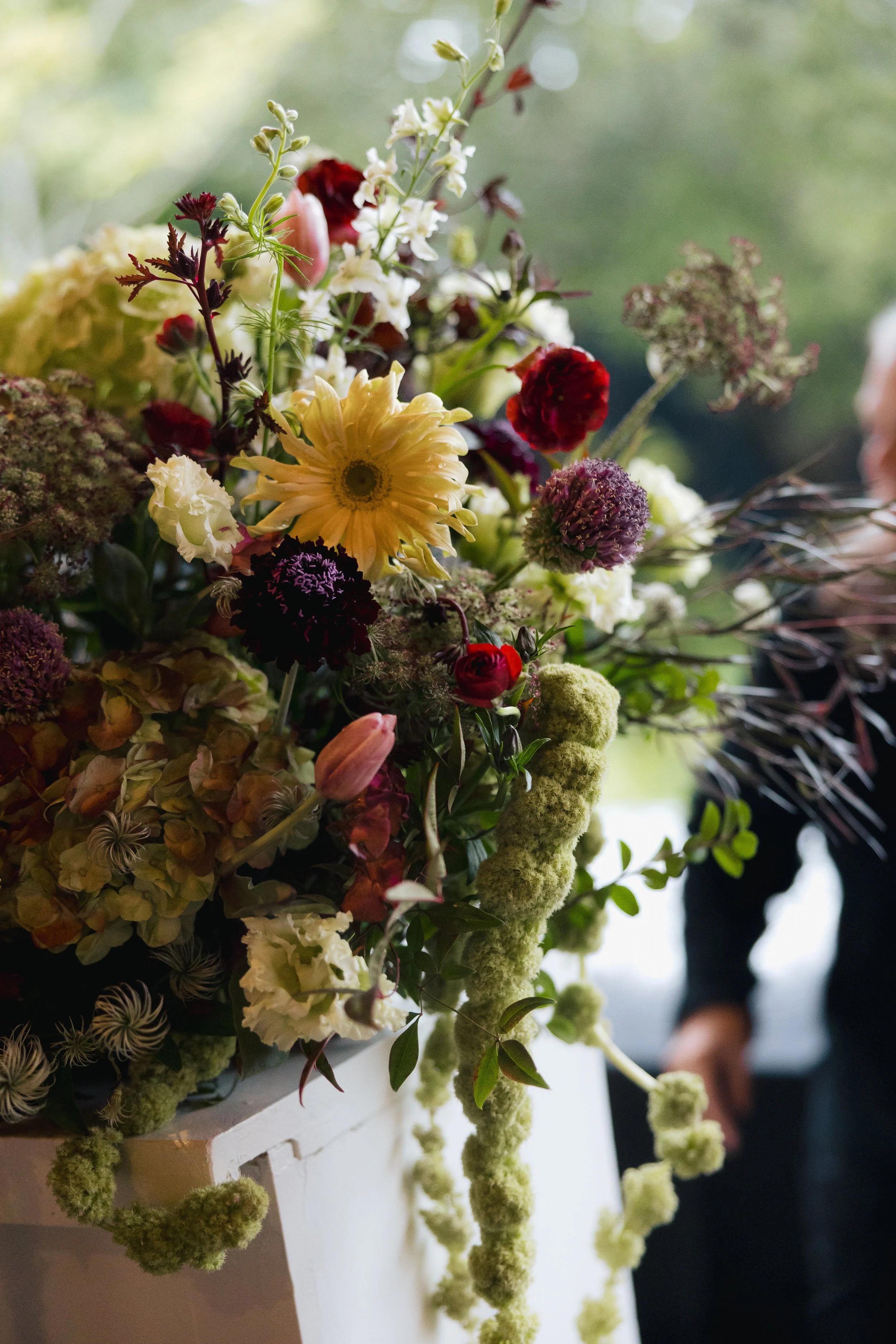 Moody garden-style wedding floral arrangement featuring layered blooms in deep red, soft yellow, ivory, and cascading greenery designed by Ivory & Beau.