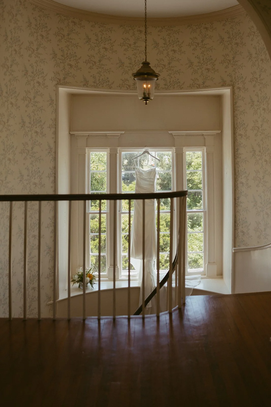 Bride’s wedding dress hanging in historic window at Agapae Oaks on St. Helena Island South Carolina, elegant Southern bridal preparation scene at Lowcountry destination wedding venue.
