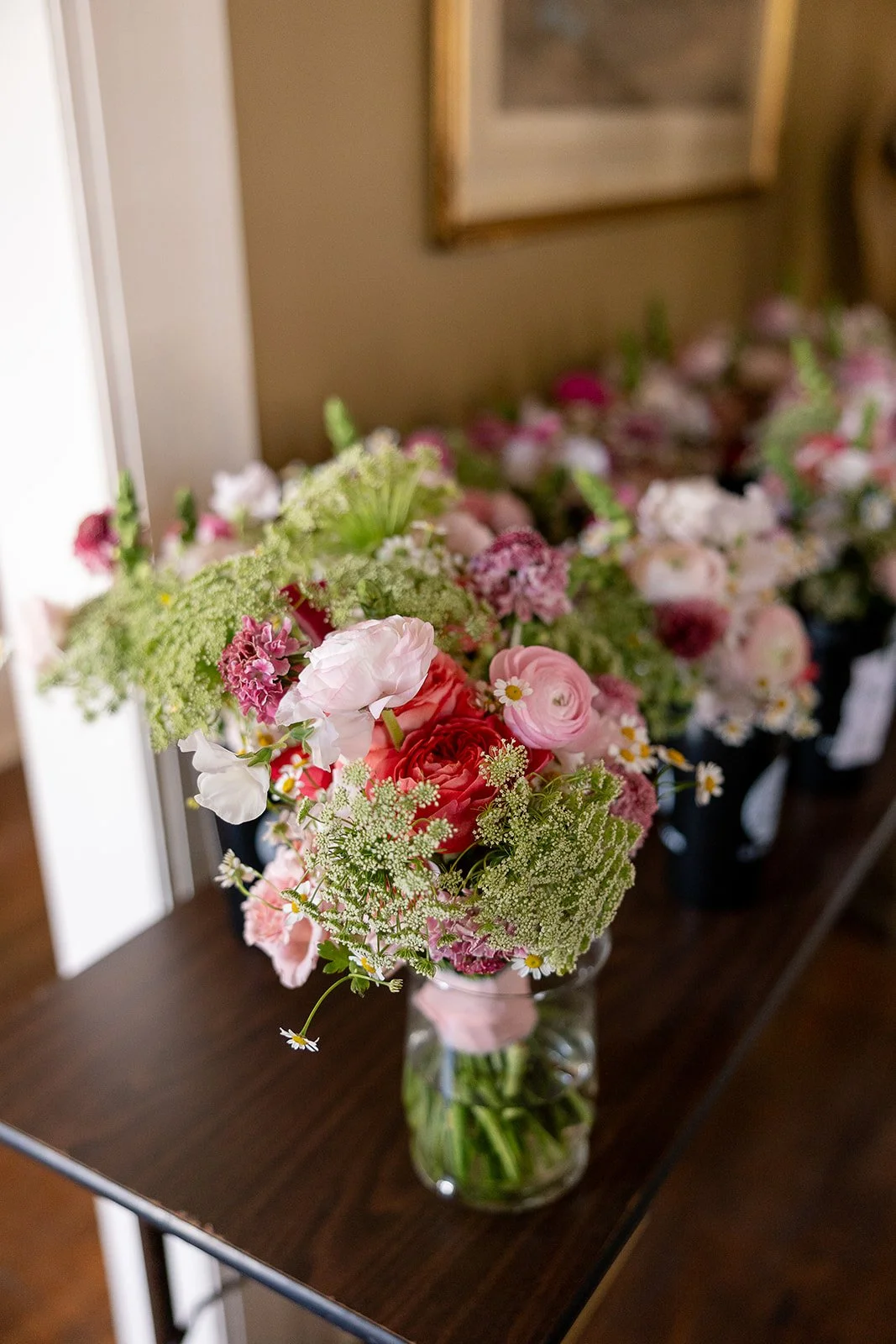 A bouquet of pink, white, and red flowers in a glass vase on a dark wooden table.