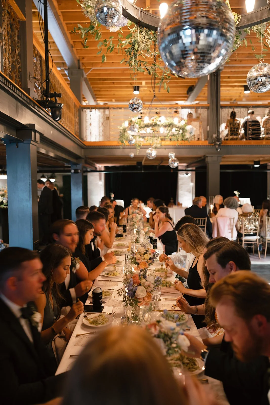 Wedding reception dinner at Victory North Savannah Georgia with long guest table, floral centerpieces, hanging greenery and disco balls, designed by Savannah wedding florist for modern industrial destination wedding.