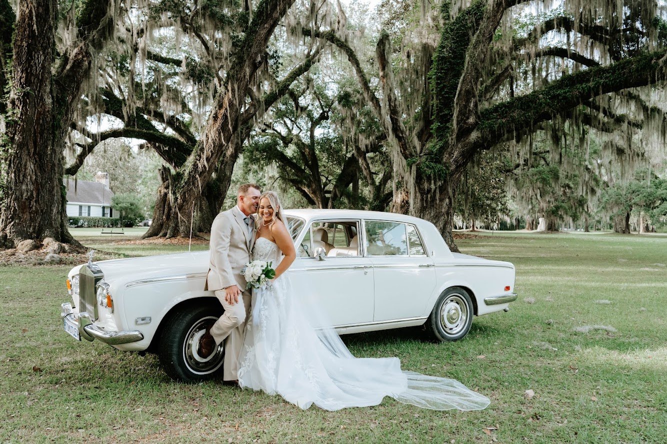 Bride and groom posing with a vintage Rolls-Royce beneath Spanish moss.