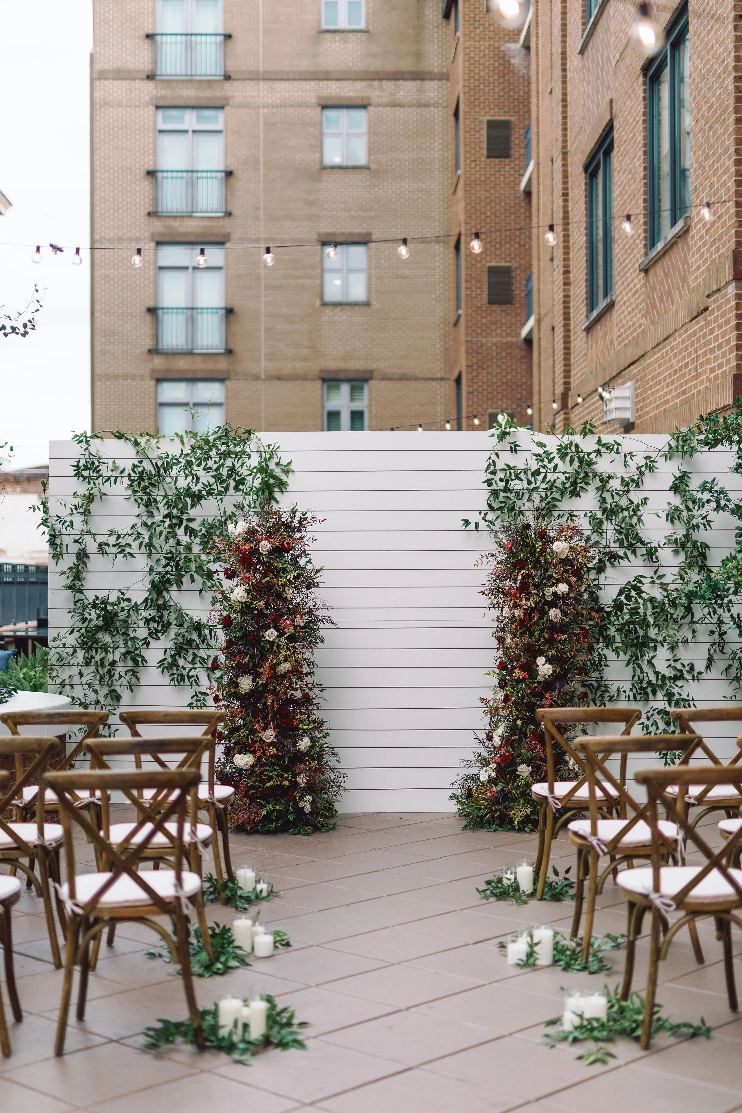 Rooftop wedding ceremony at Andaz Savannah Georgia featuring lush floral ceremony pillars, romantic aisle candles and greenery backdrop designed by Savannah wedding florist for downtown destination wedding.
