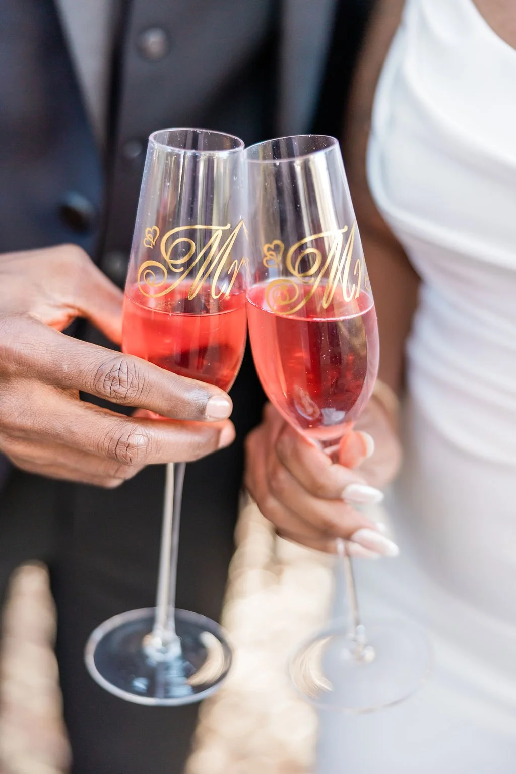 Two people clinking champagne glasses with pink-colored beverage, each glass labeled 'Mr.' and 'Mrs.' in gold script.