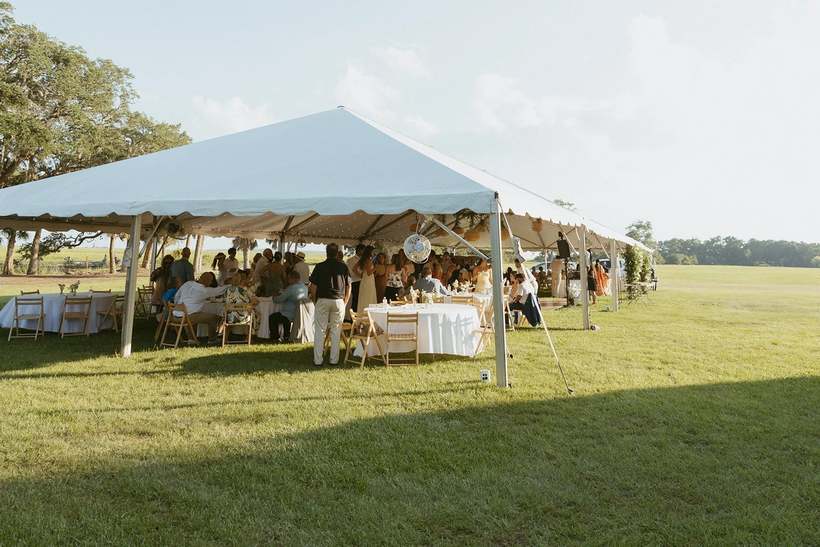 Outdoor tented wedding reception at Agapae Oaks on St. Helena Island South Carolina featuring large sailcloth-style reception tent, guest seating and scenic Lowcountry destination wedding setting.
