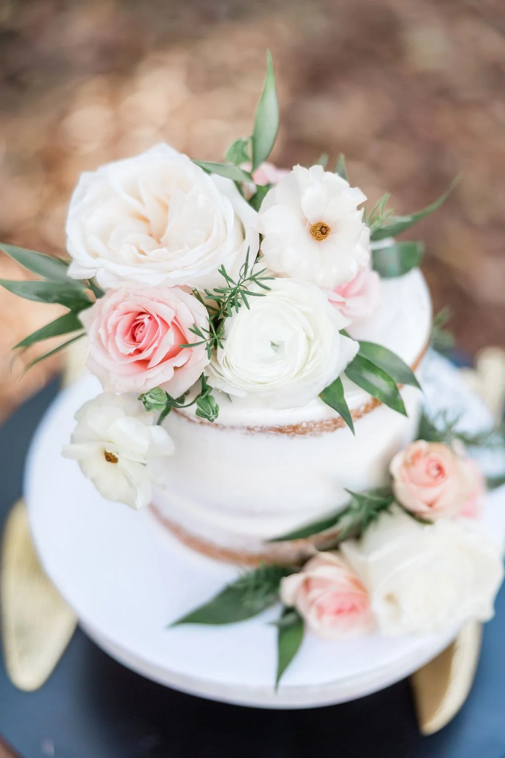 A layered white wedding cake decorated with white and light pink roses, white ranunculus flowers, and green foliage.
