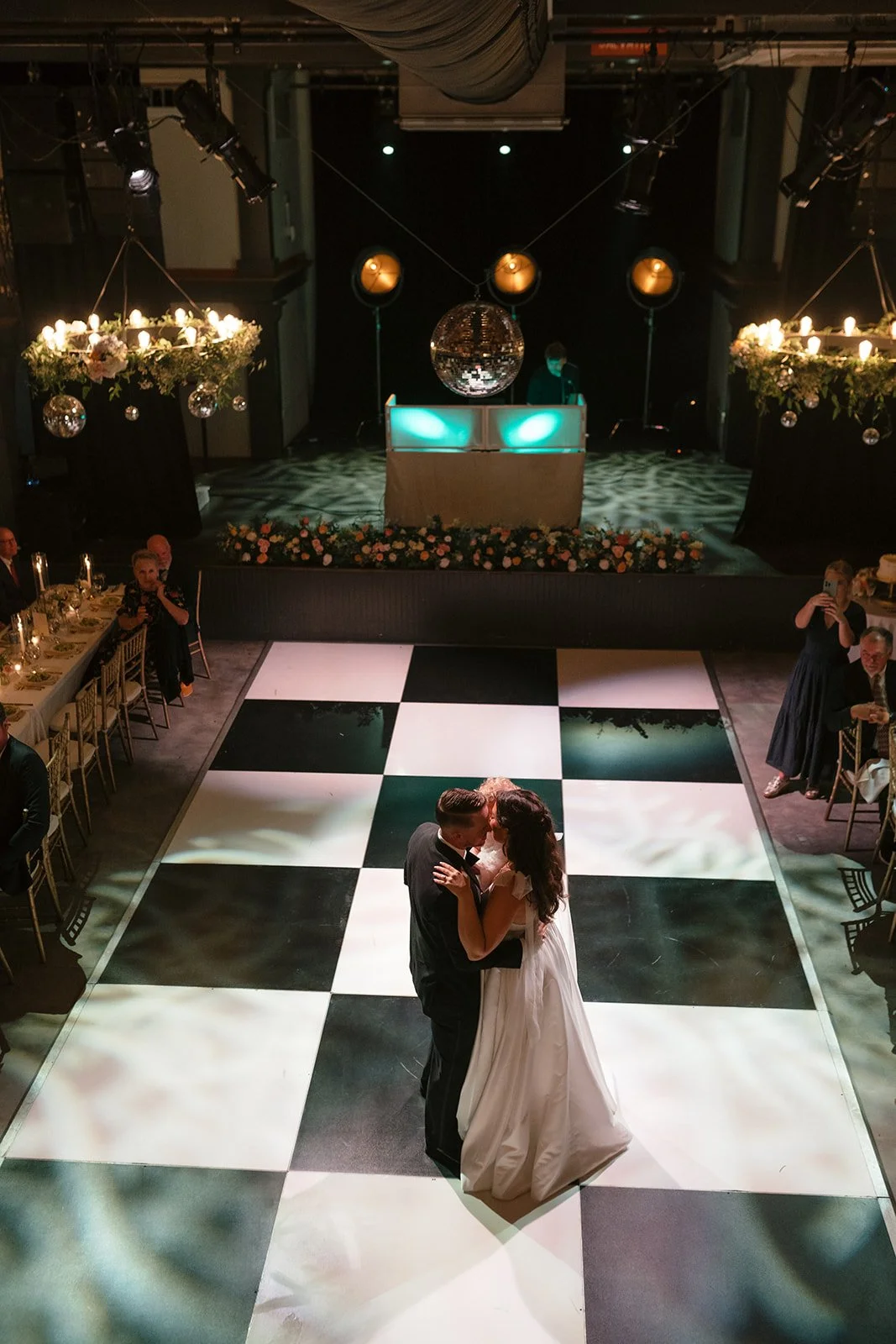 Bride and groom first dance at Victory North Savannah Georgia wedding venue with dramatic lighting, stage DJ setup, floral installations, and modern industrial reception design by Savannah destination wedding florist.