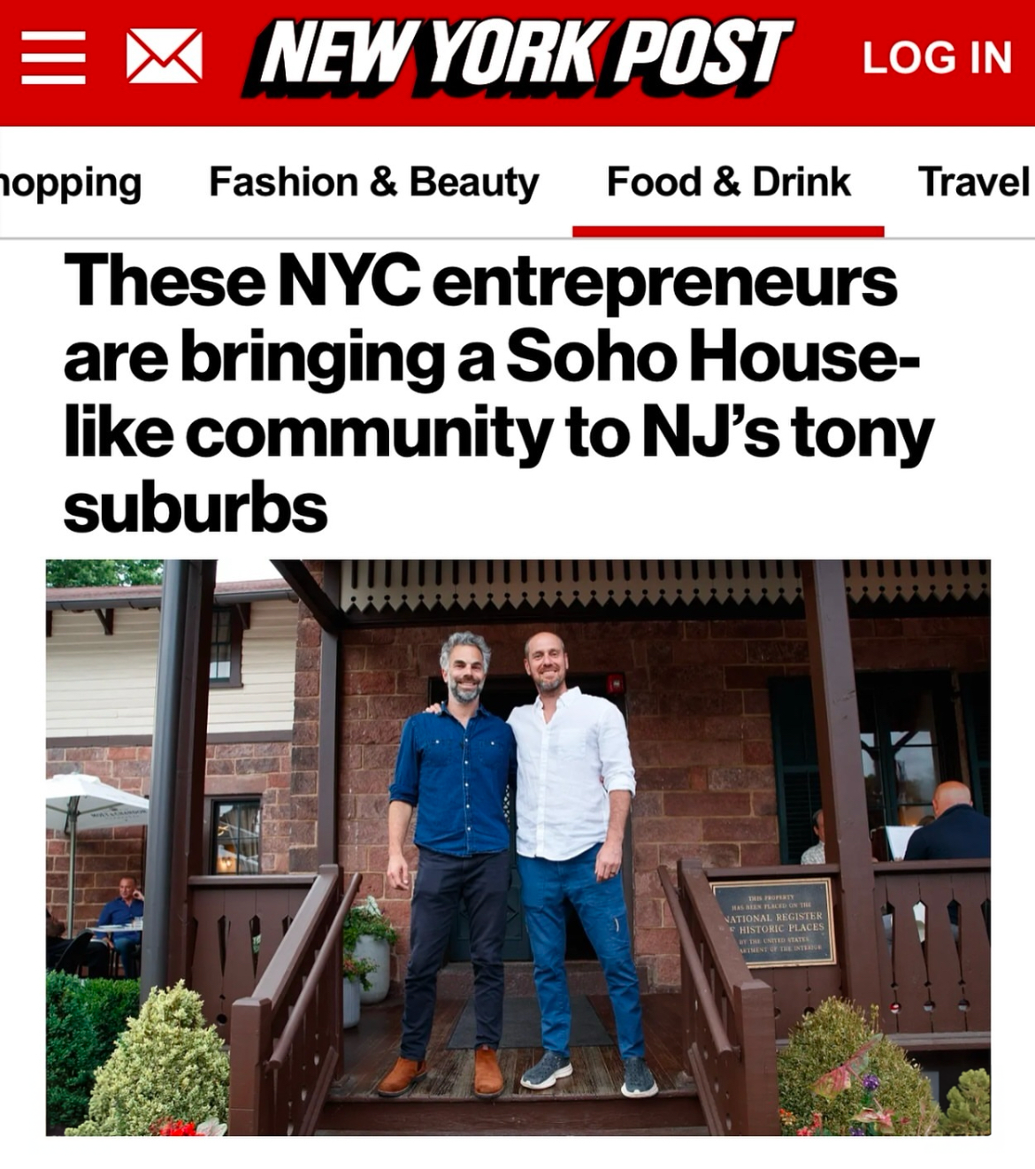 Two men standing outside a community house, smiling at the camera, with a brick building and porch in the background.
