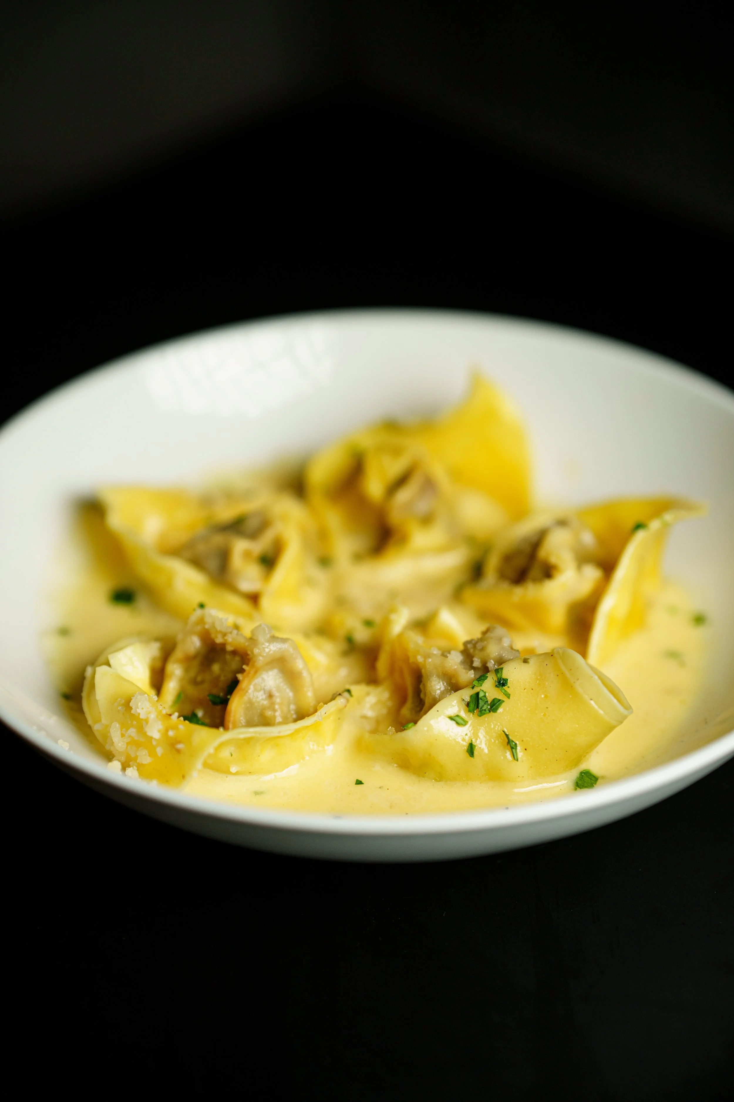 A serving of lasagna on a fork, showing layers of pasta, cheese, meat, and tomato sauce, with more lasagna in a brown dish in the background.