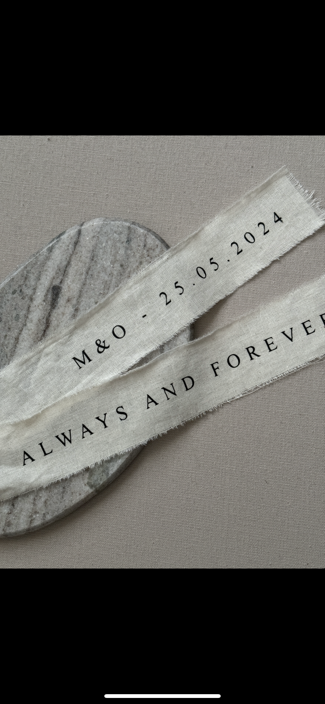 Deux rubans en tissu blanc avec inscriptions en noir, posés sur une pierre plate en marbre. Le premier ruban porte la date "25.05.2024" et le second message "ALWAYS AND FOREVER".