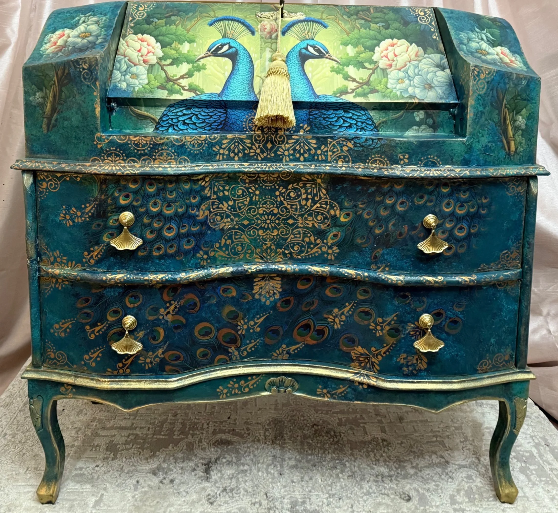 A hand-painted blue and gold jewelry box with peacock and floral designs, featuring a gold tassel on top.