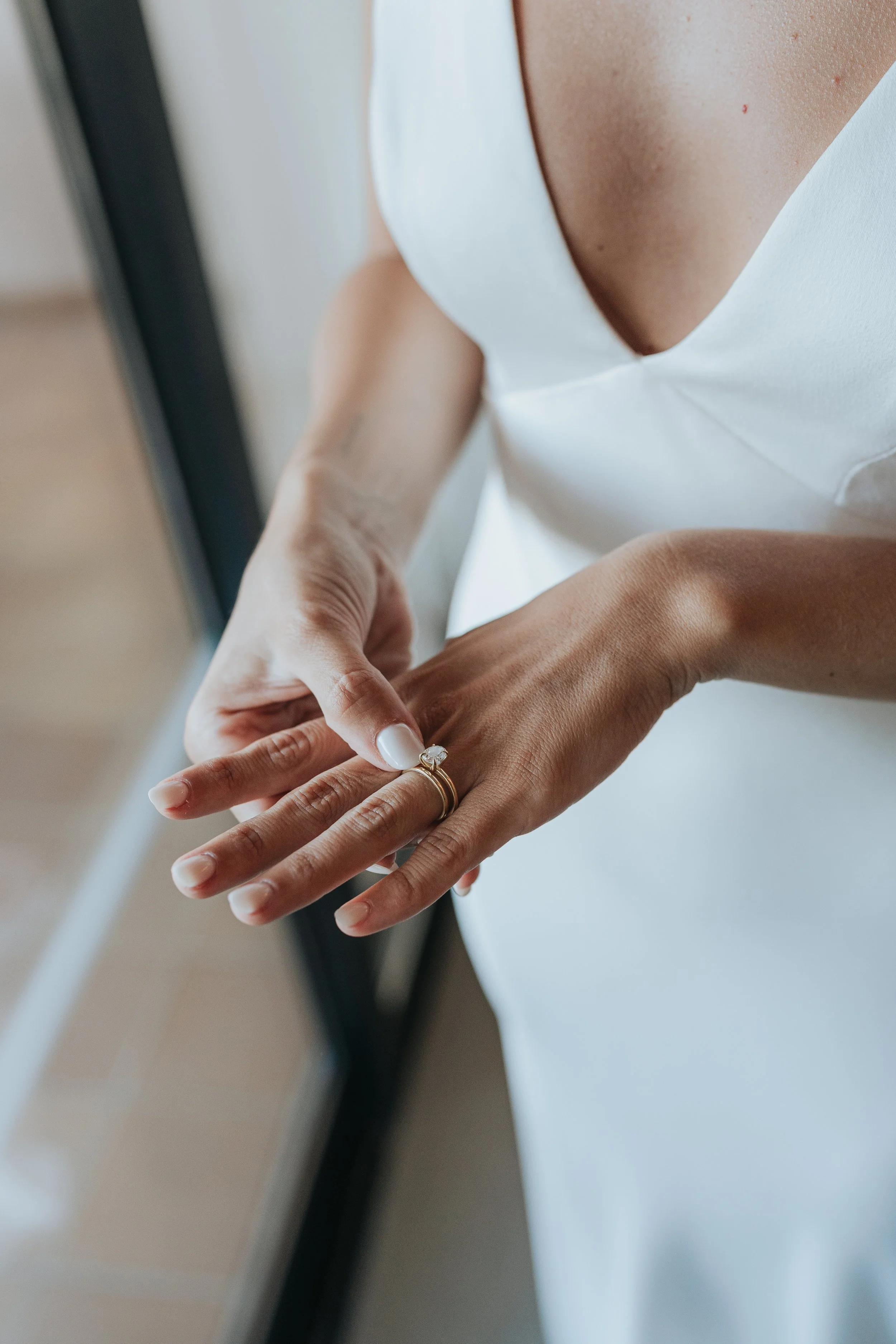 A person wearing a white top with a deep V neckline, holding the hand of another person who is wearing a ring on their finger.