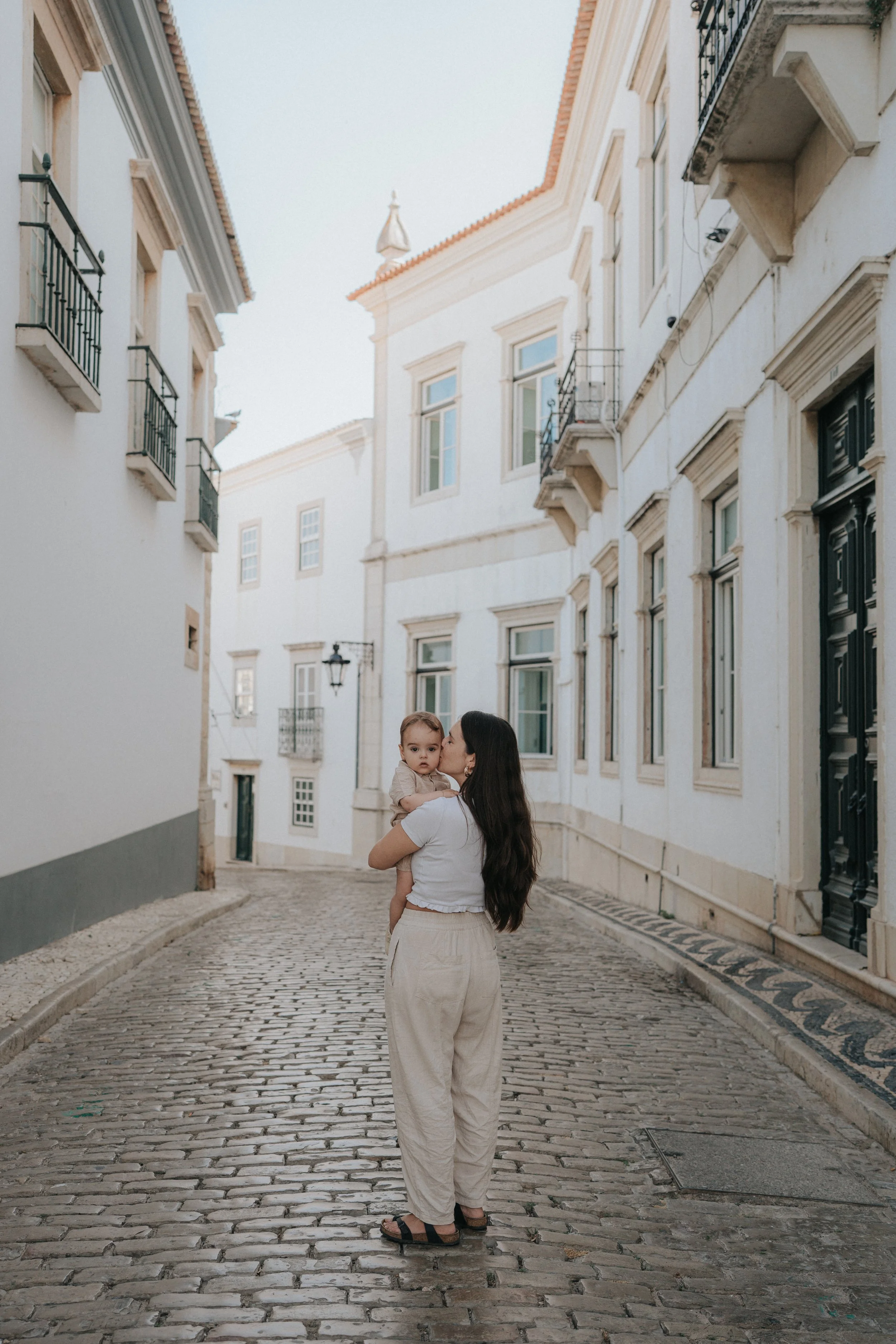 Woman holding a child standing on a cobblestone street in a European style neighborhood.
