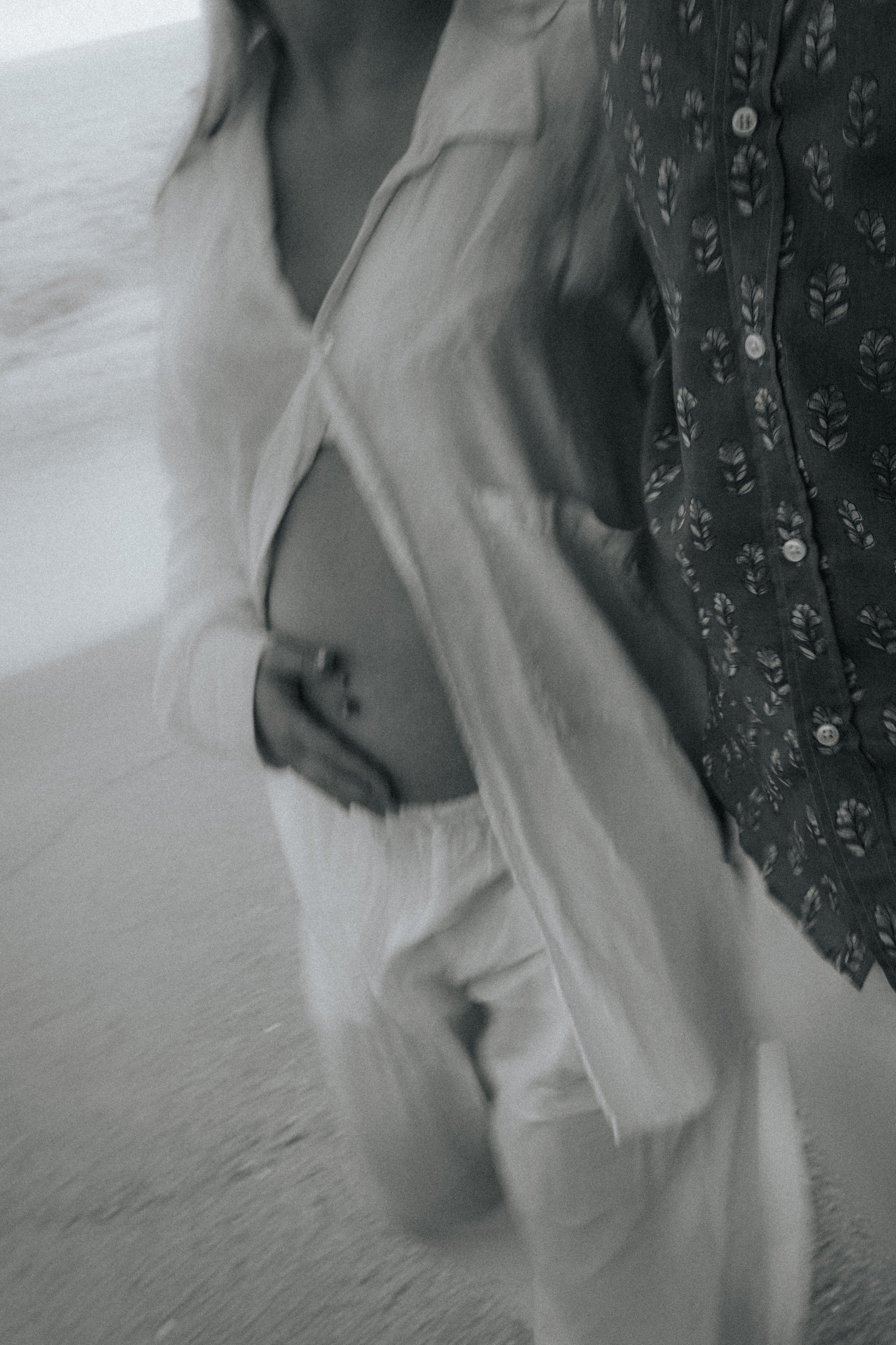 Close-up of a person's arm wearing a patterned shirt and light-colored pants, with the fabric partially folded, lying on a wooden surface.