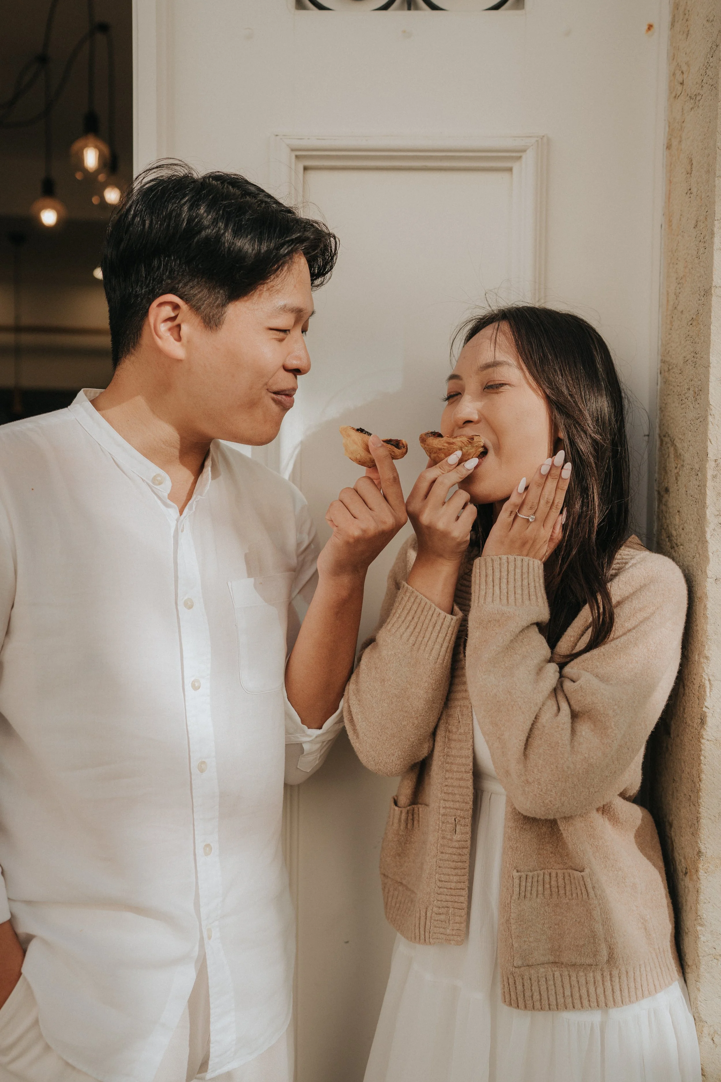 A man and woman sharing a moment indoors, holding slices of pizza and smiling at each other.