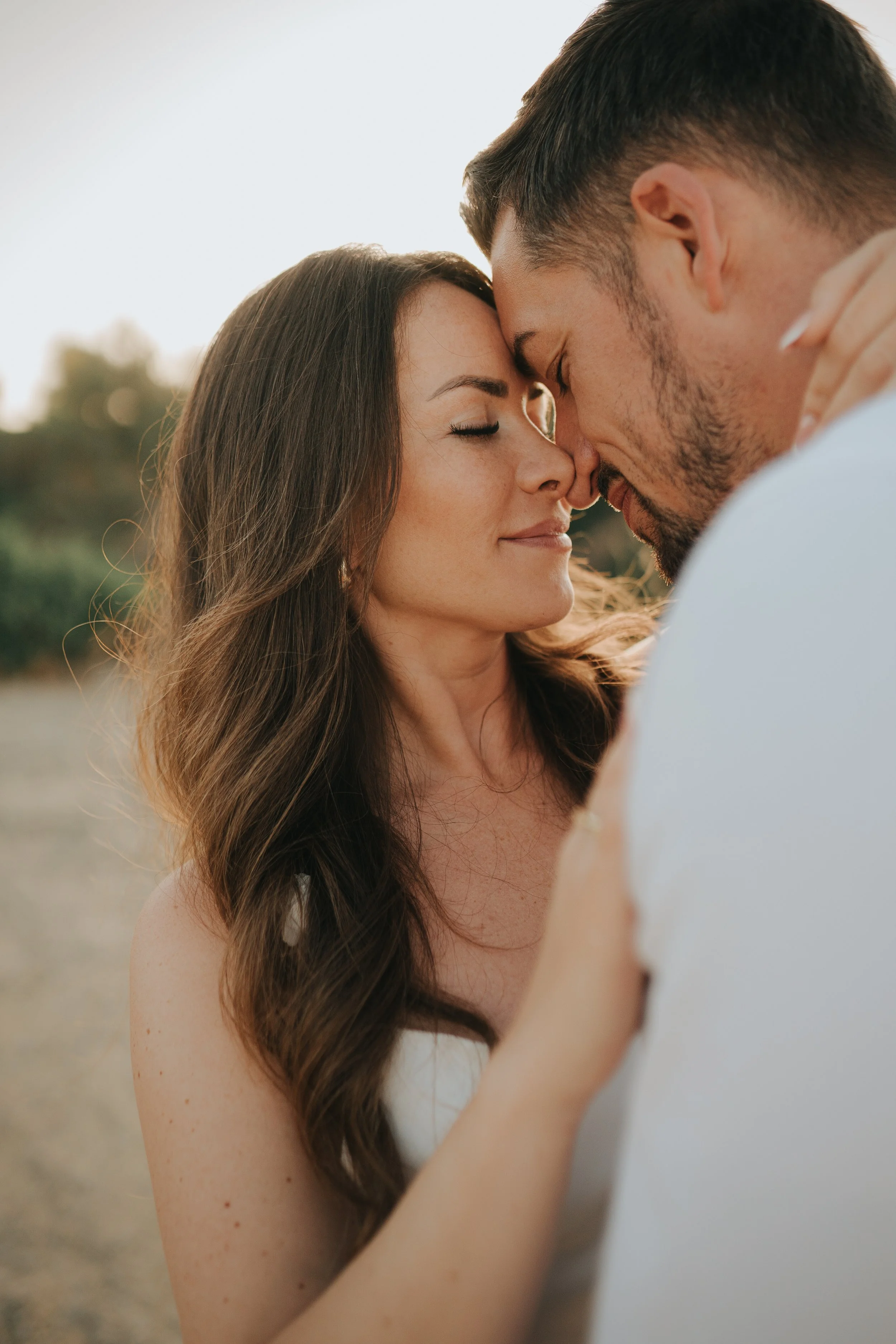A couple with close faces touching, eyes closed, outdoors, with blurred natural background.