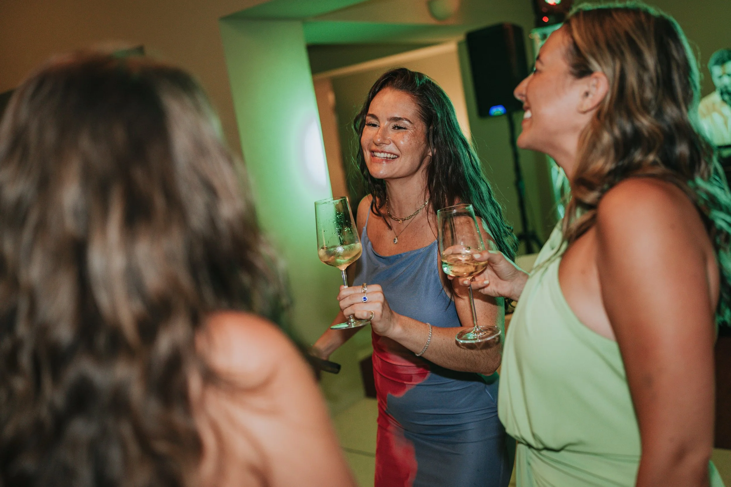 Women celebrating with glasses of white wine at a party, smiling and engaging in conversation.