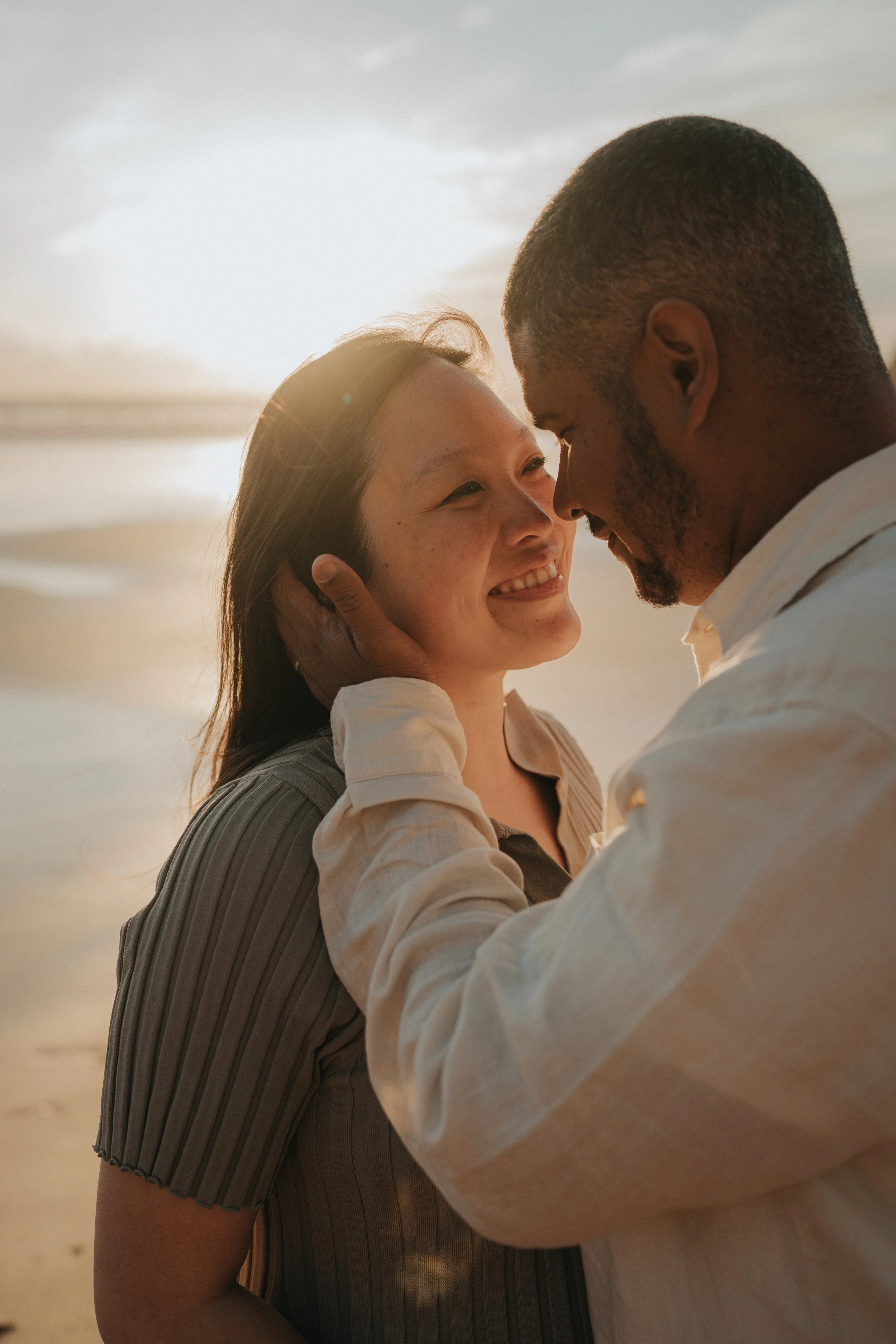 A couple on the beach with the sunset in the background, sharing an intimate moment and touching foreheads.