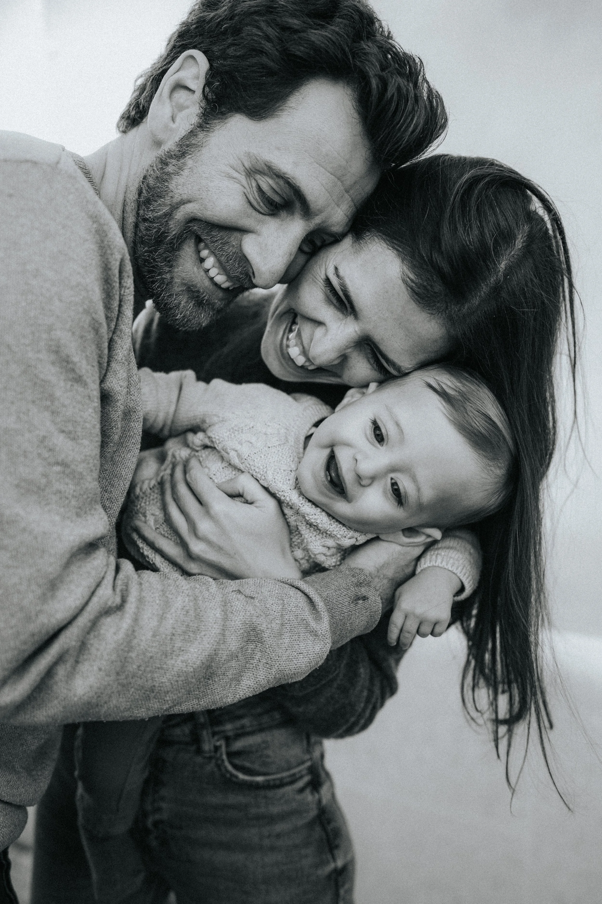 A happy family moment with a man, woman, and child sharing a close embrace and smiling in black and white.