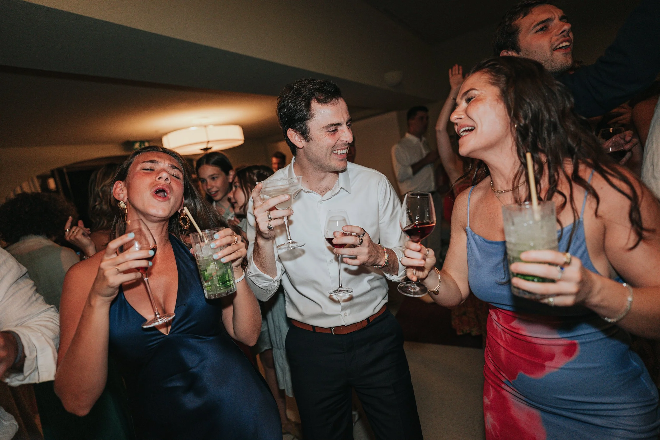 People dancing and enjoying drinks at a party in a dimly lit room.