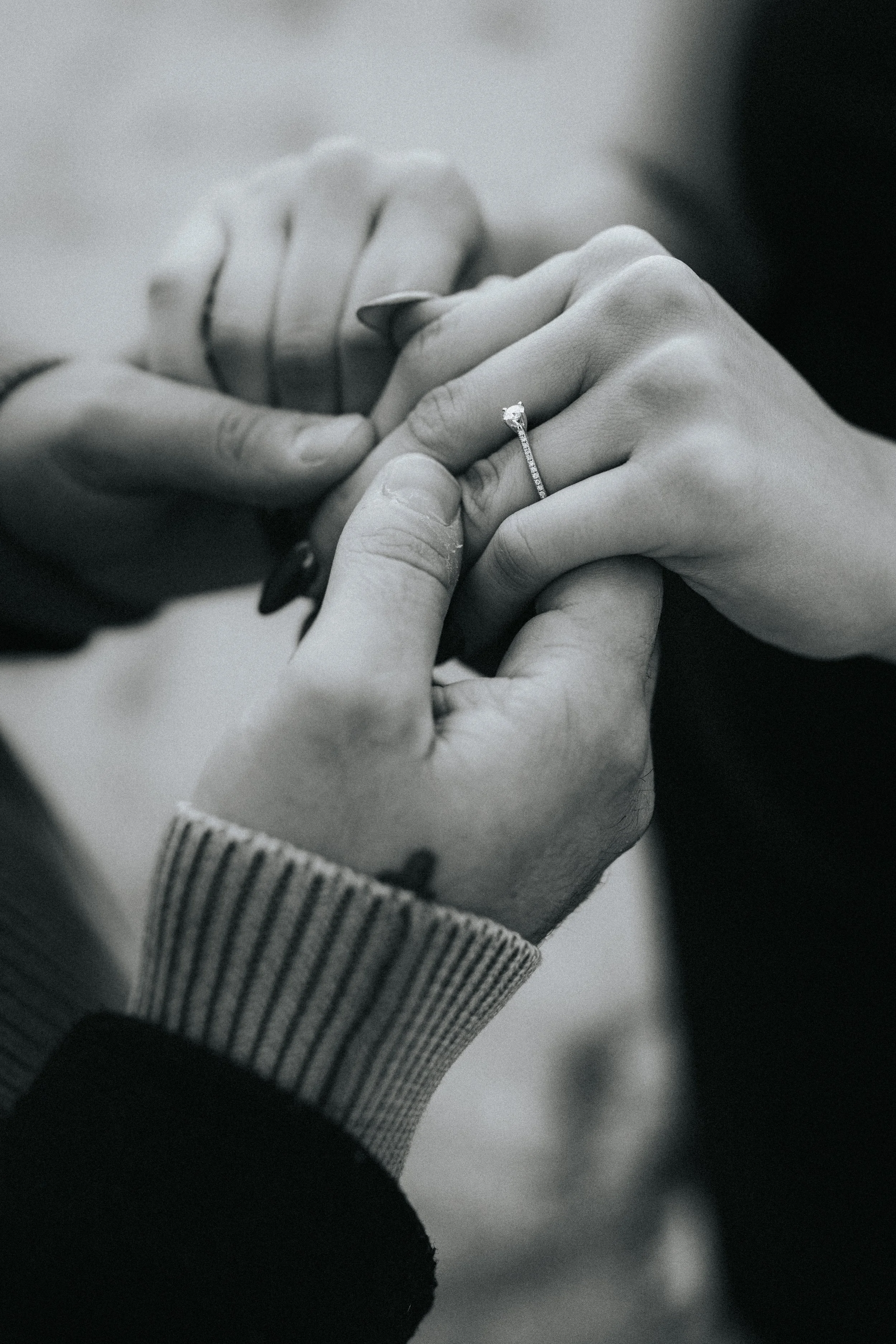A black and white photo of two hands, one with a ring on the ring finger, holding and touching each other.
