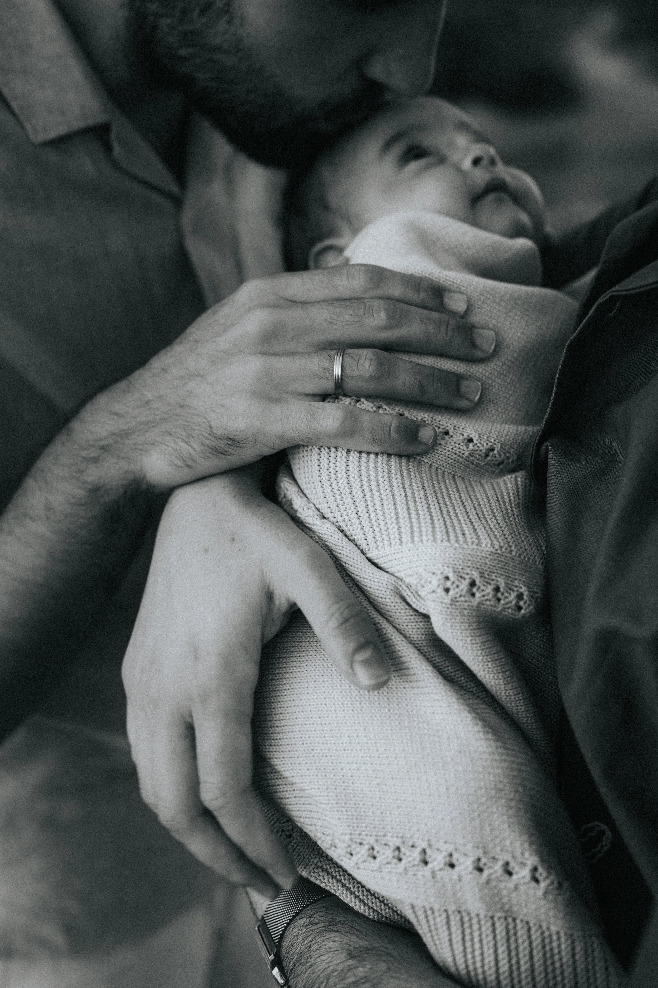 A man is holding a smiling baby in his arms, close to his face. The man is cuddling the baby, and their faces are touching. The baby is looking up happily. The photo is in black and white.